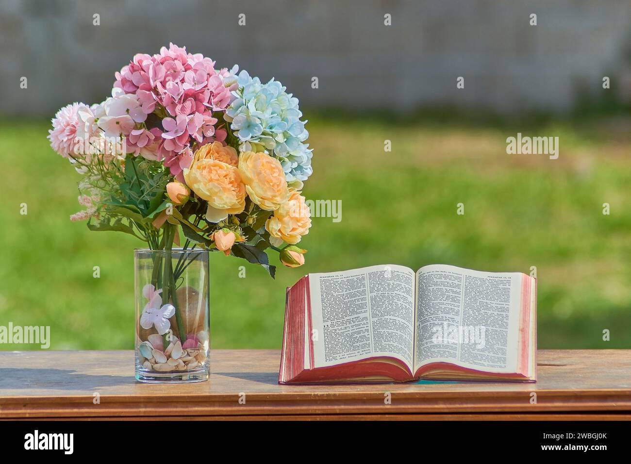Offenes Bibelbuch mit Blumen in verschiedenen Farben daneben. Die Bibel steht auf einem Medera-Tisch, Hintergrund ist unscharf. Christliches Konzept Stockfoto