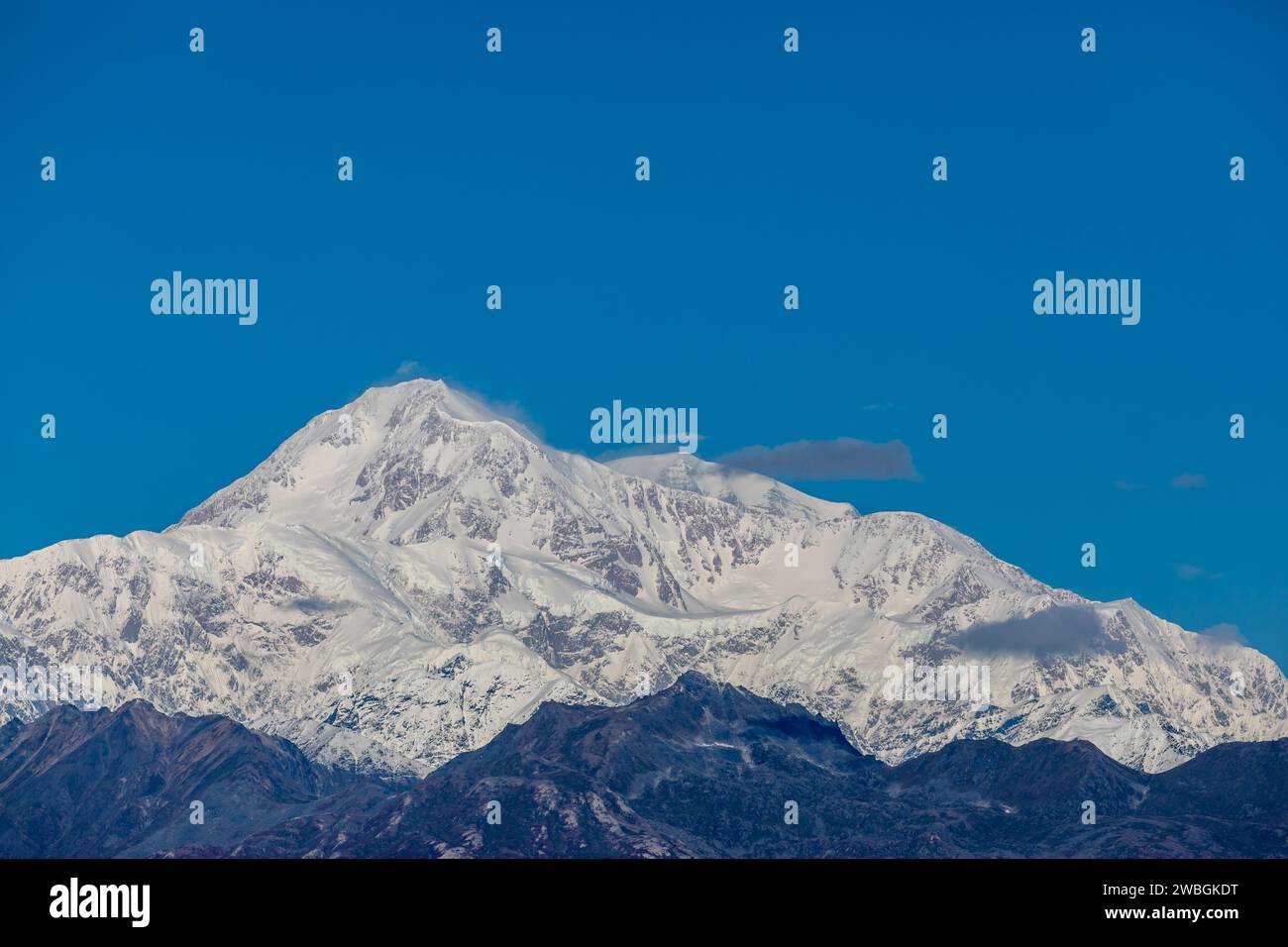 Der massive, schneebedeckte Denali-Gipfel erhebt sich über den dunklen Bergrücken der darunter liegenden Alaska Range Stockfoto