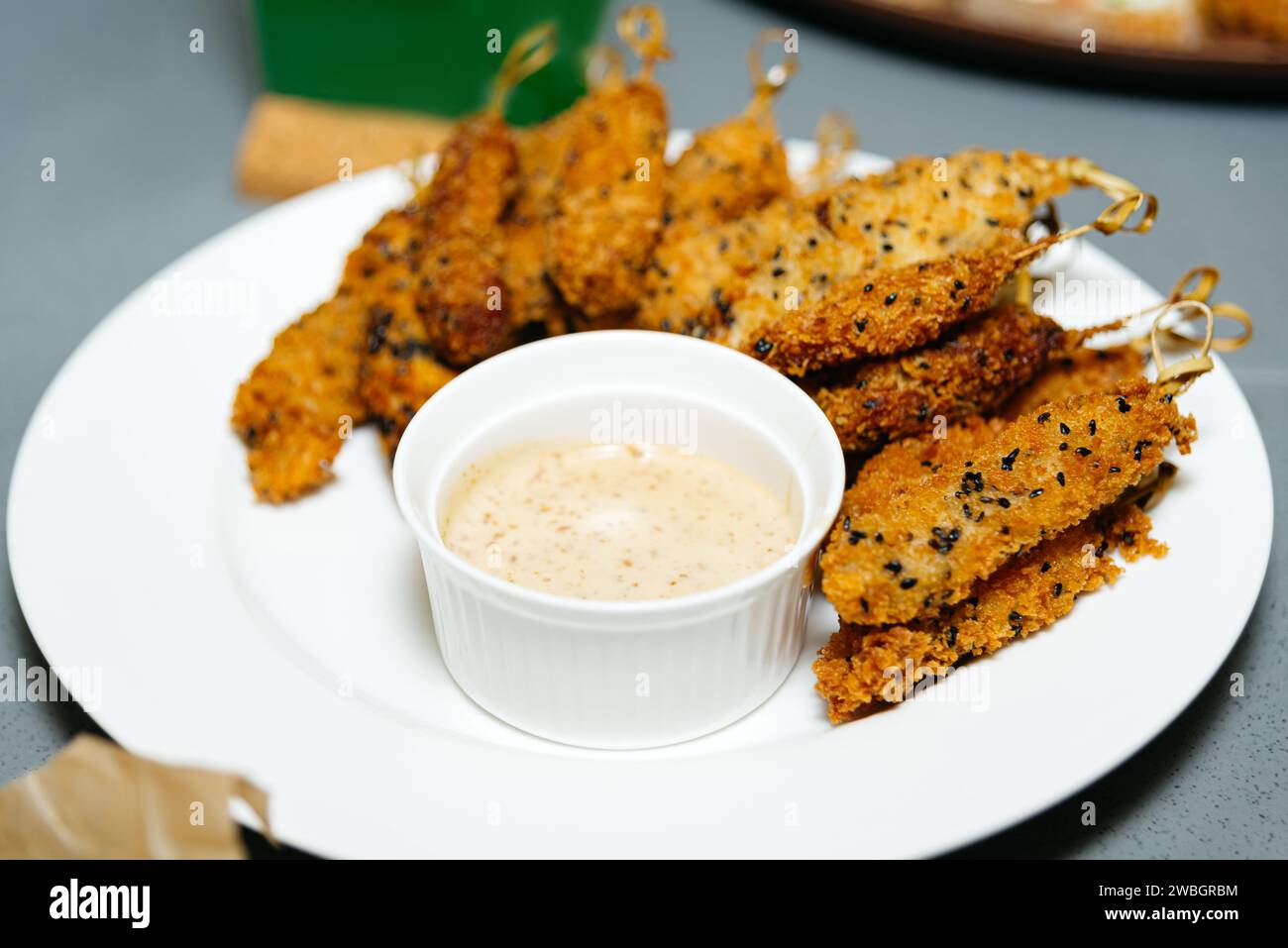 Goldene, frittierte Hähnchenstreifen mit Sesamsamen, serviert mit einem cremigen Dip auf einem weißen Teller, ideal für einen herzhaften Snack. Stockfoto