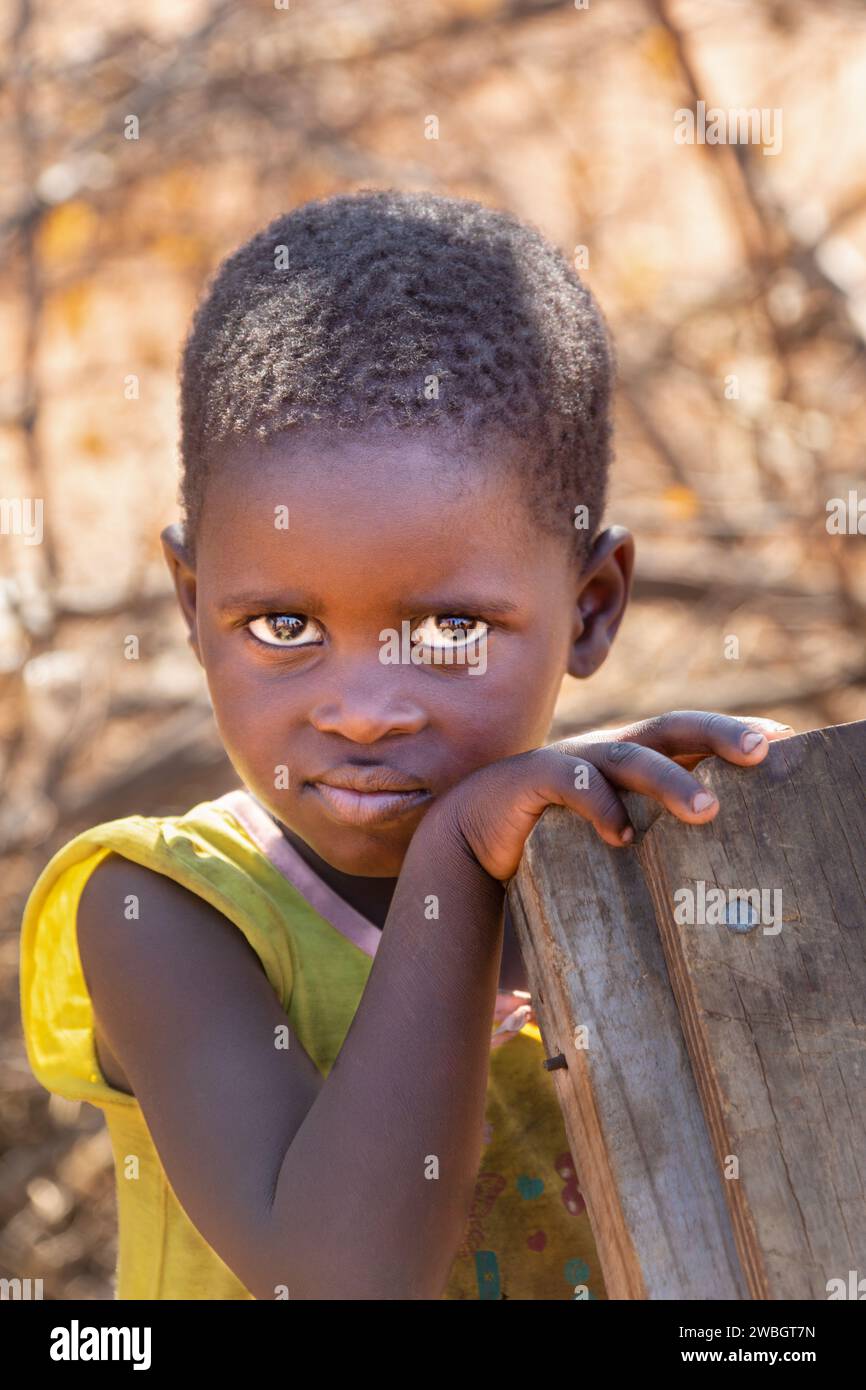 Porträt eines afrikanischen Kindes im Hof, Dorfleben, das Mädchen hält einen Holzstuhl Stockfoto