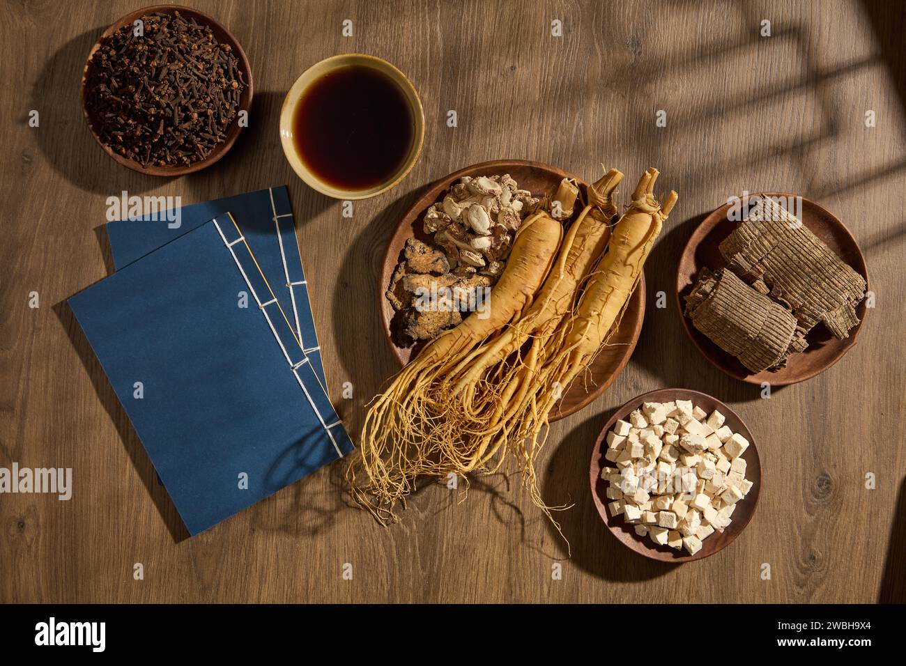 Aromatischer Ingwer, Szechuan Lovage Rhizome und Ginseng-Wurzeln auf einem runden Gericht. Zwei Bücher, eine Schüssel mit Tonic und anderen Medikamenten arrangierten aro Stockfoto