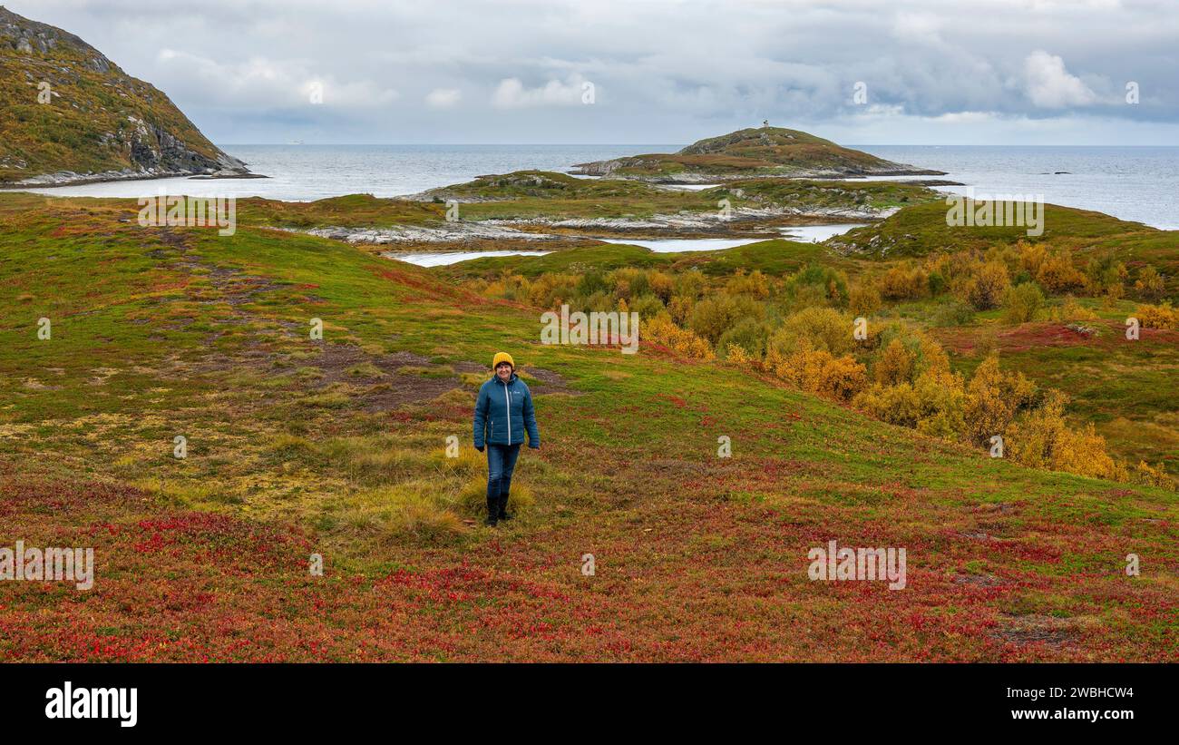 Wanderfrau in der herbstlichen Natur Norwegens. Wandern am Fjord und den Bergen auf der Insel Kvaløya, Troms, grüne, orange und rote Pflanzen Stockfoto