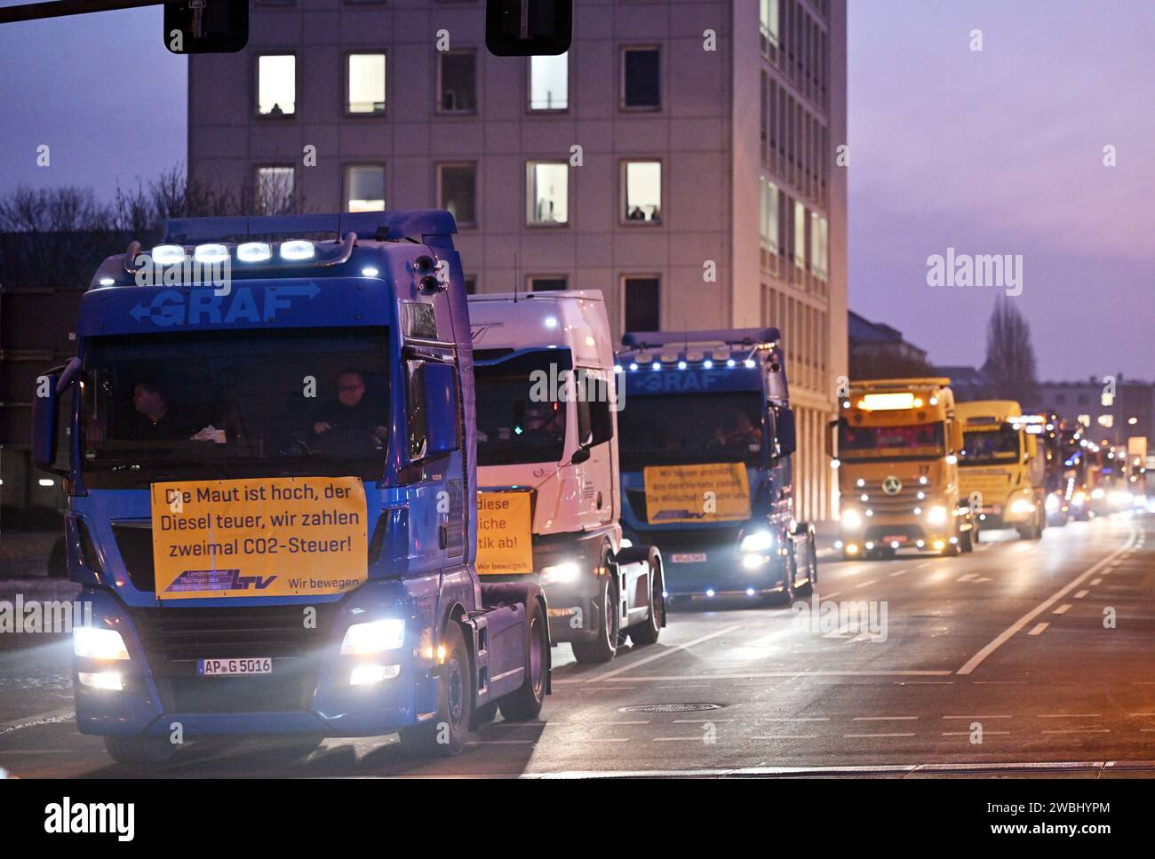 Erfurt, Deutschland. Januar 2024. Lkw mit Banner fahren im Konvoi am Thüringer landtag vorbei. Neben den protestierenden Bauern hat auch die staatliche Transportindustrie einen Konvoi gestartet. Die Spediteure wollten gegen die Doppelbelastung der Lkw-Maut und der CO2-Abgabe protestieren. Rund 150 Fahrzeuge nahmen an dem Protest Teil. Der rund fünf Kilometer lange Konvoi rollte von Erfurt über Weimar nach Jena. Quelle: Martin Schutt/dpa/Alamy Live News Stockfoto