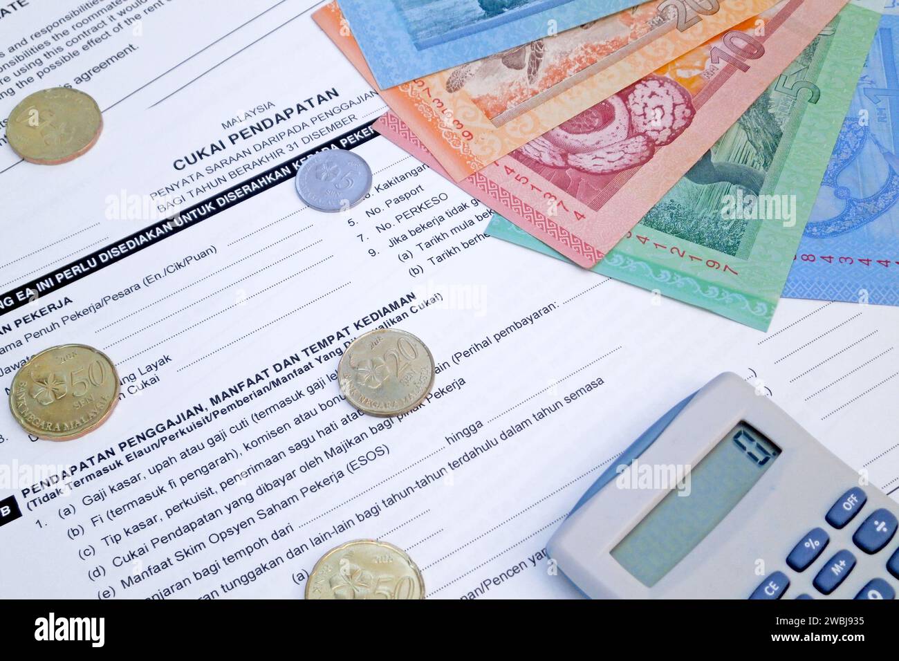 Ein Taschenrechner und einige Ringgit-Münzen und -Banknoten auf einem malaysischen Einkommensteuerformular. Stockfoto