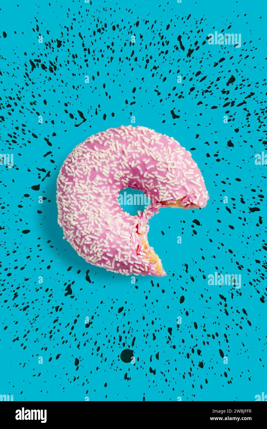 Ein gebissener rosafarbener Donut mit weißen Streuseln auf blauem Hintergrund. Frischer Donut mit rosafarbener Glasur. Stockfoto