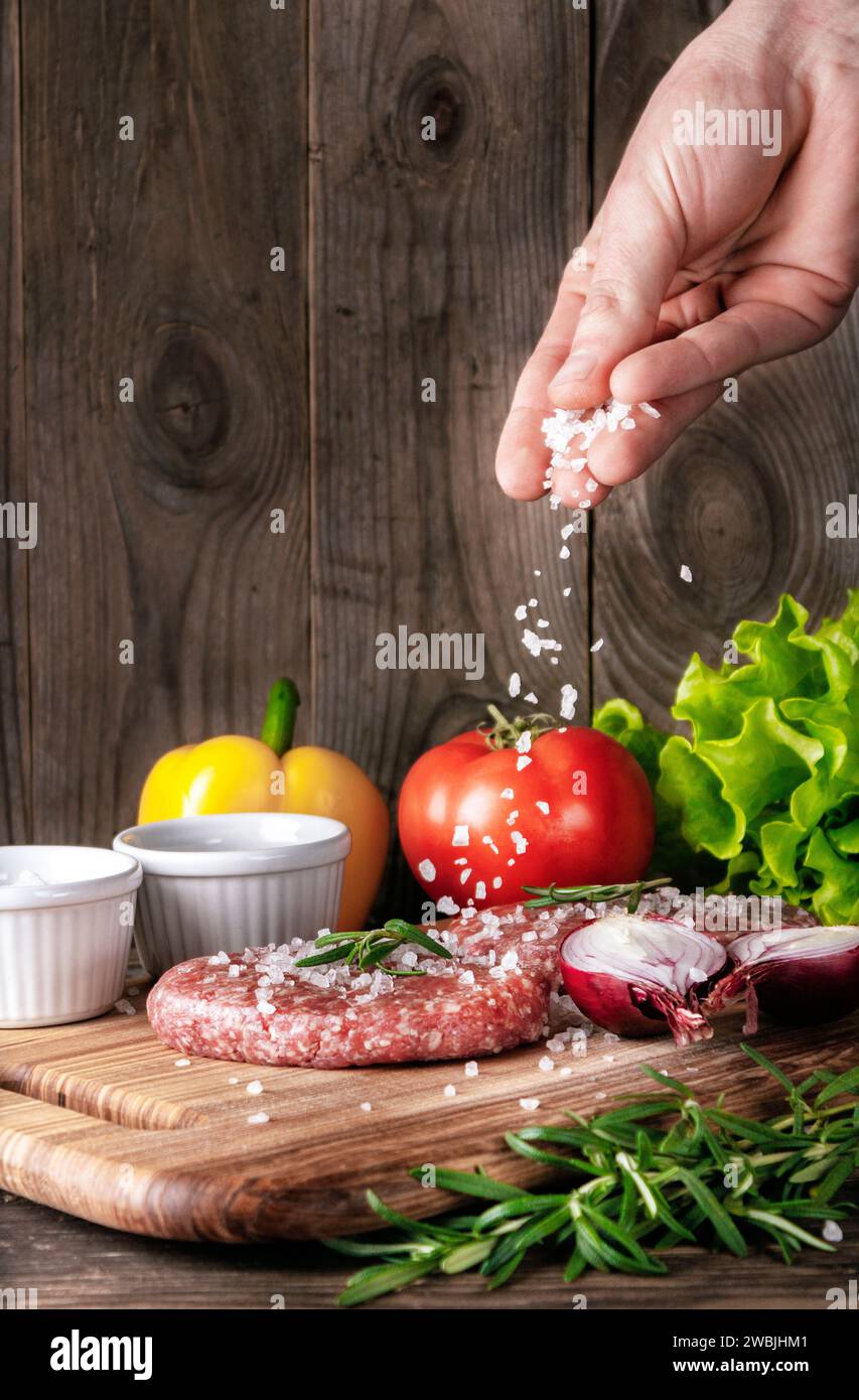 Rohe Bio-Fleischkoteletts. Kochen Sie Salz auf Fleischkoteletts auf einem hölzernen Schneidebrett. Zubereitung von Fleisch für einen köstlichen hausgemachten Hamburger. Stockfoto