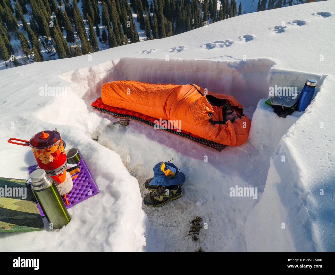 Ein Mann schläft in einem Schlafsack in einem verschneiten Tierheim. Mehrtägige Wanderungen in den Bergen im Winter. Winterüberleben in den Bergen Stockfoto