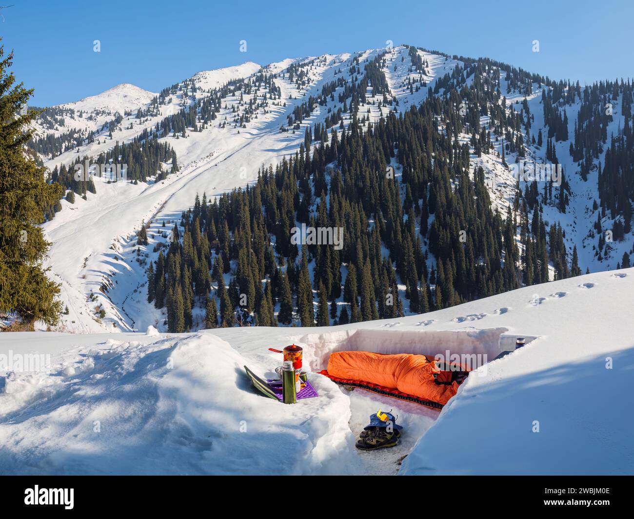 Übernachtung in den Bergen im Winter. Ein Mann schläft in einem Schlafsack in einem verschneiten Tierheim. Mehrtägige Wanderungen im Winter Stockfoto