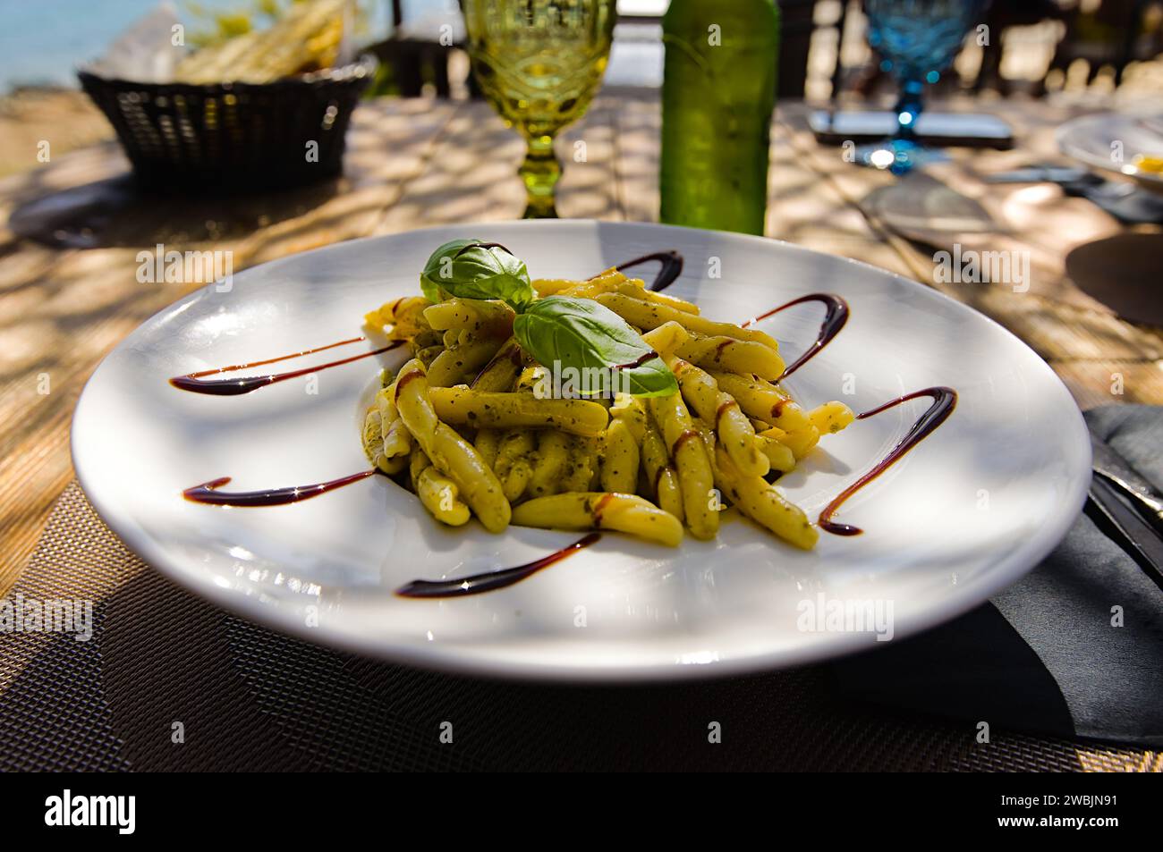 Penne Pasta auf einem weißen Teller auf Sardinien, mit Pesto, Balsamico-Essig und frischen Basilikumblättern. Stockfoto