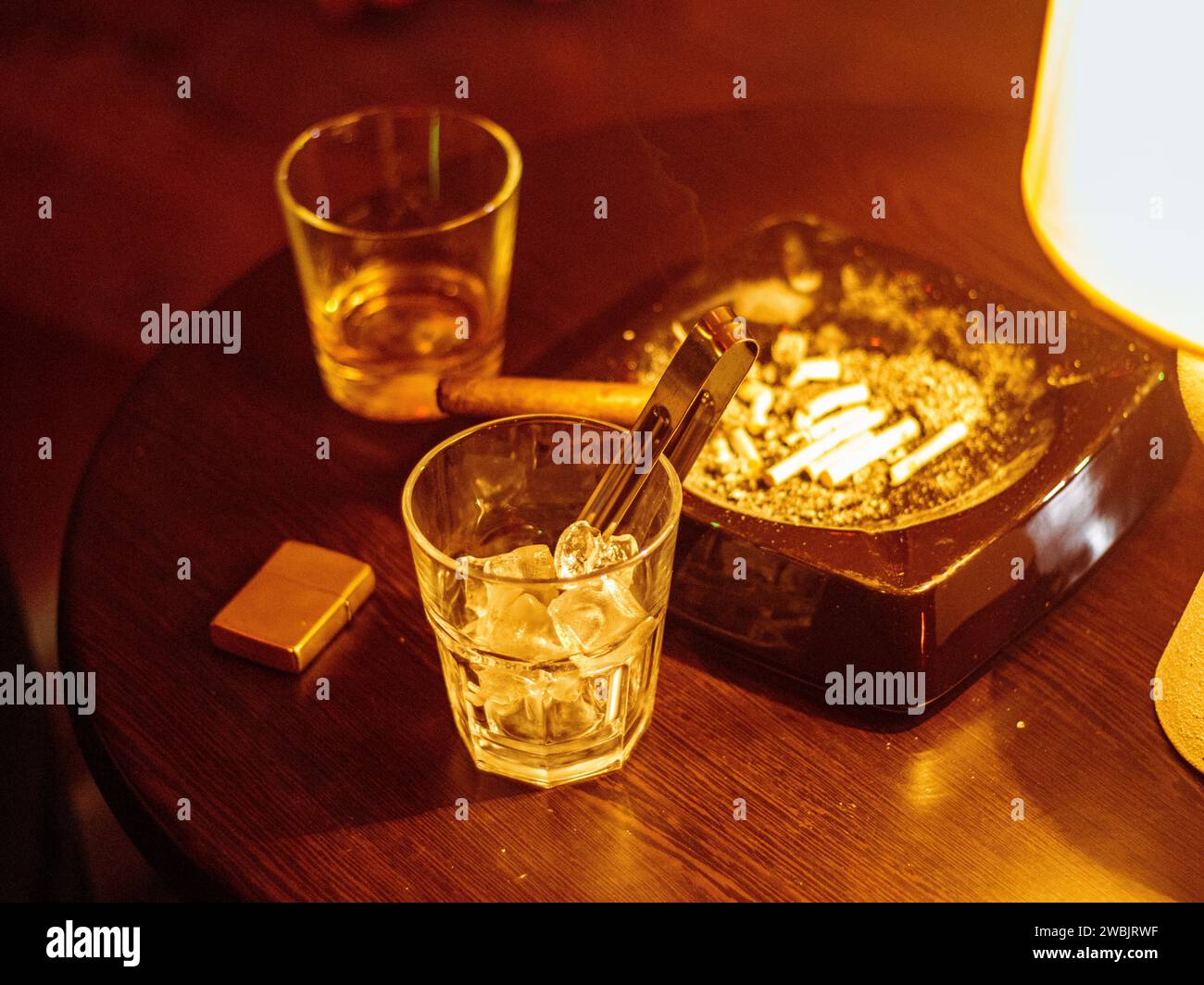 Glas Whiskey mit rauchender Zigarre und Eiswürfeln auf Holztisch Stockfoto