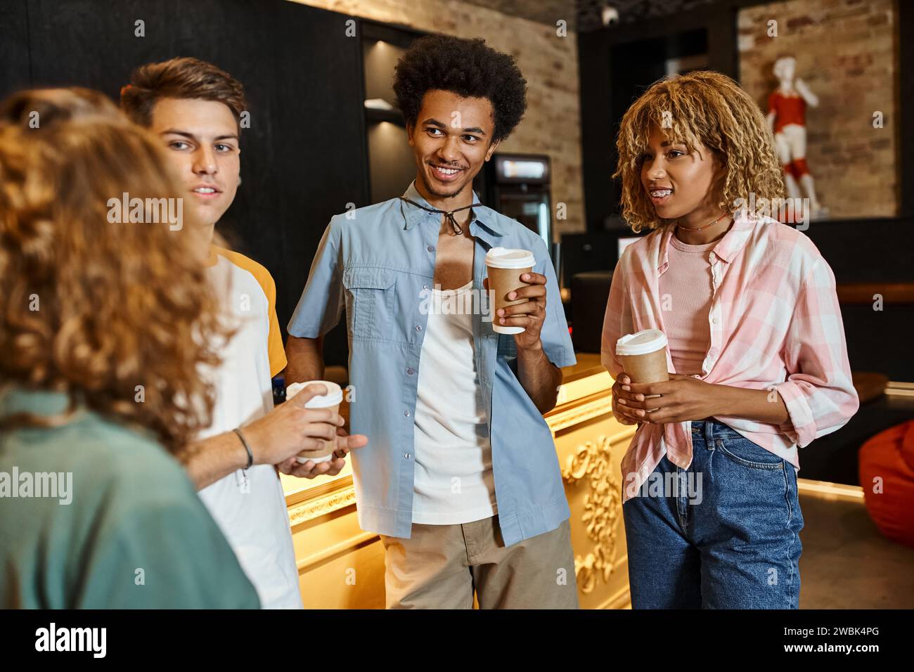Fröhliche multiethnische Freunde mit Pappbecher unterhalten sich an der Rezeption in der Jugendherberge, Reisende Stockfoto