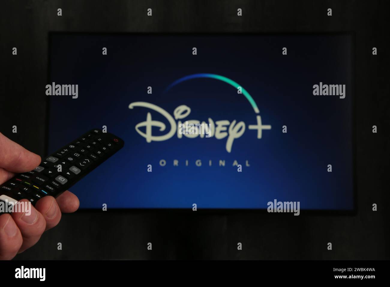 Nikolaev, Ukraine - 20. November 2021. Iman mit TV-Fernbedienung in der Hand und Disney Logo Hintergrund. Draufsicht. Stockfoto