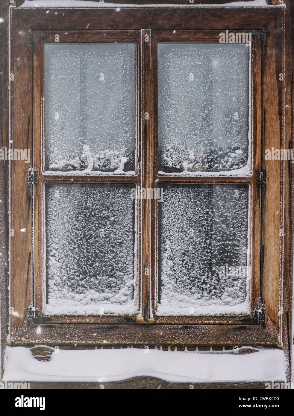 Schneebedecktes altes Holzfenster mit gefrorener Scheibe Stockfoto