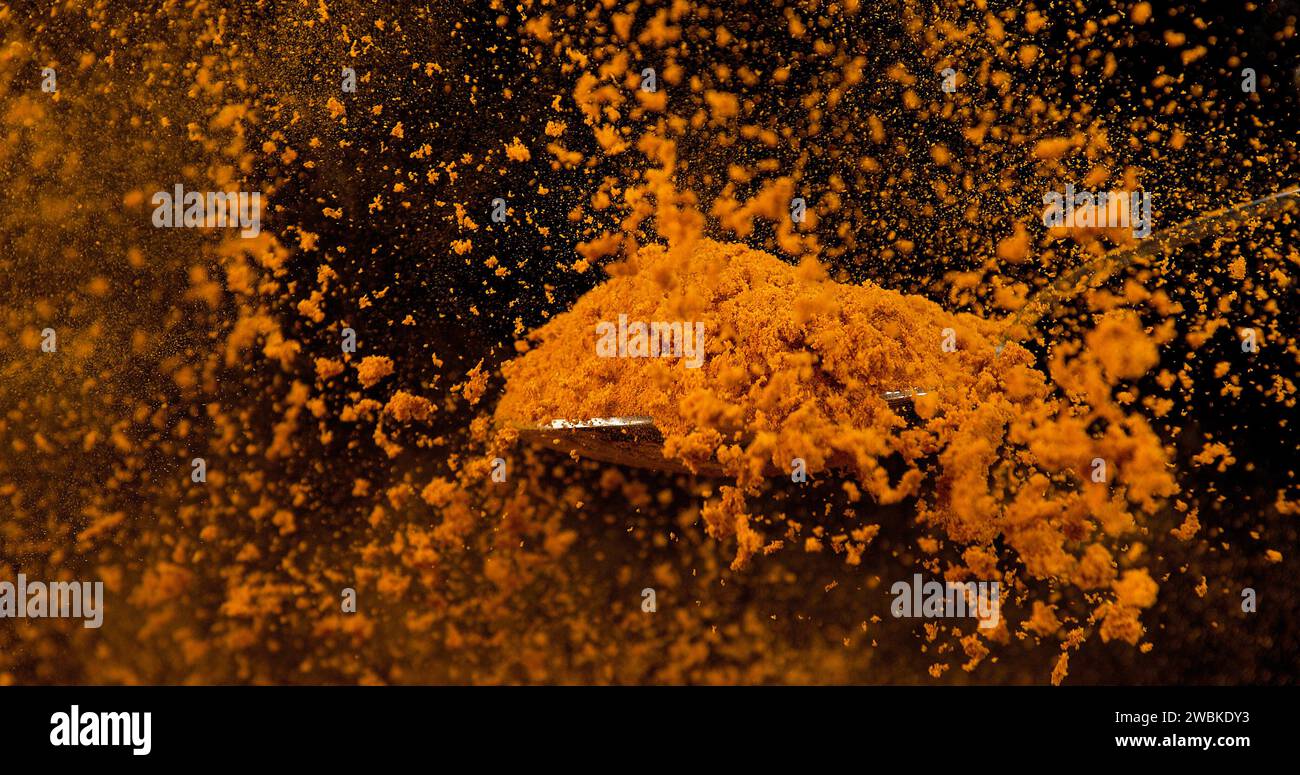 Löffel und Currypulver fallen aus Löffel vor schwarzem Hintergrund Stockfoto