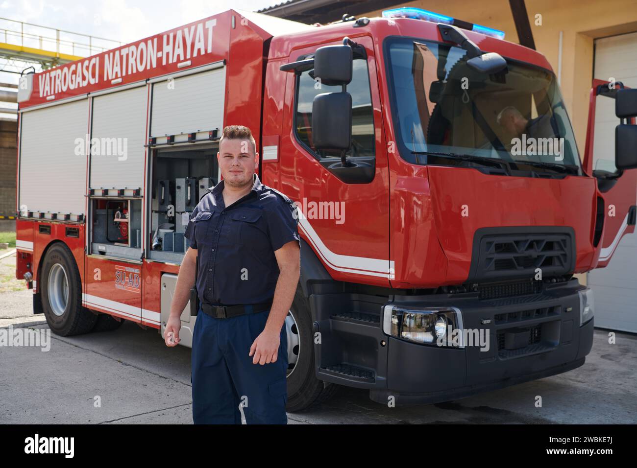 Ein selbstbewusster Feuerwehrmann posiert vor einem modernen Feuerwehrauto und strahlt Stolz, Stärke und Bereitschaft für Notfallmaßnahmen aus Stockfoto