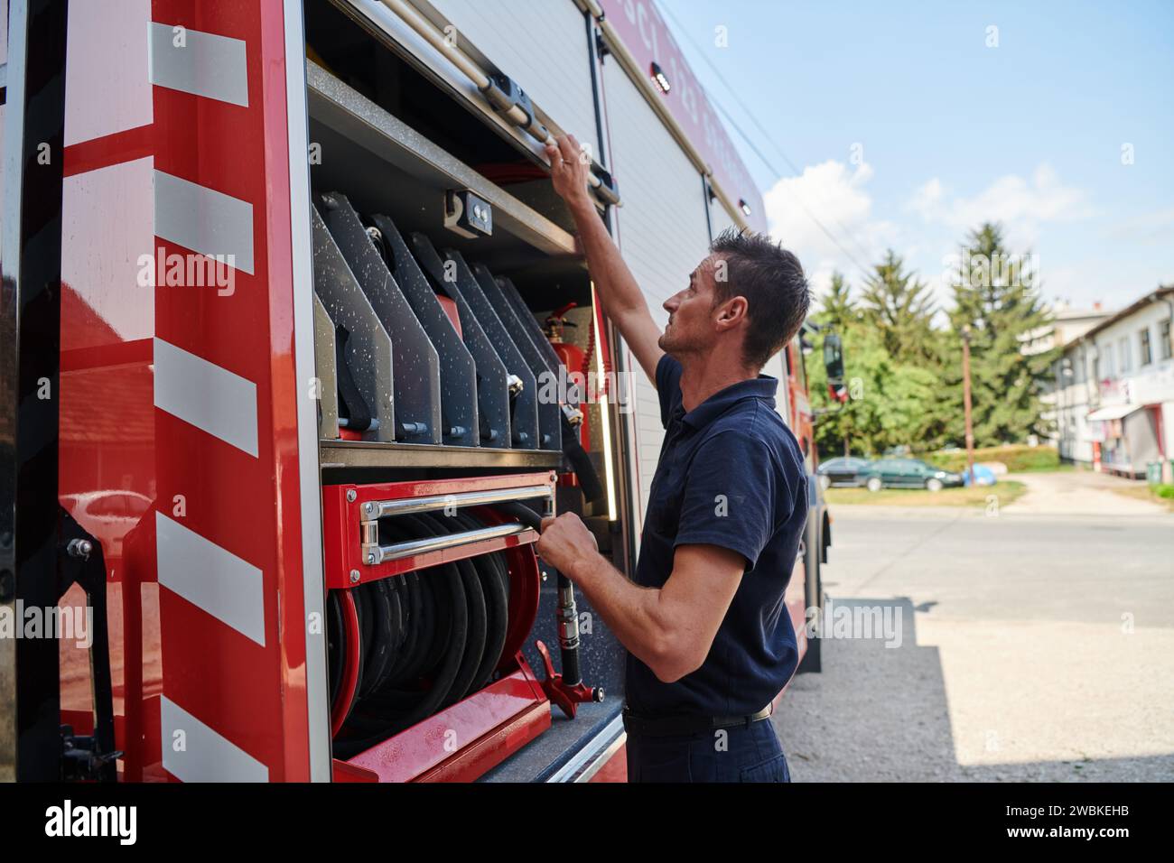 Ein dedizierter Feuerwehrmann bereitet einen modernen Feuerwehrwagen für den Einsatz in gefährdeten Bereichen vor, in denen ein Brand geschädigt wird, und demonstriert damit Bereitschaft und Engagement Stockfoto