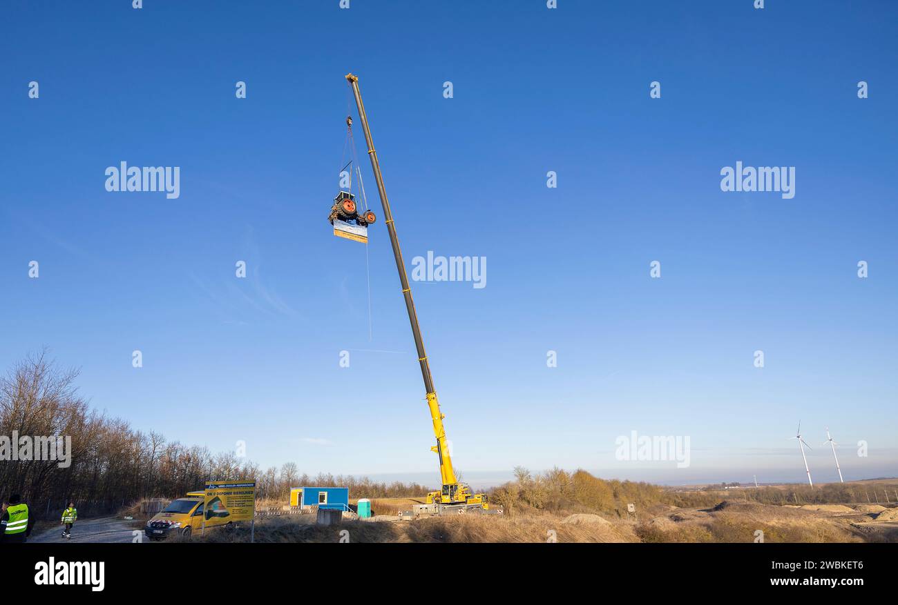 Mainstockheim, Deutschland. Januar 2024. Ein Traktor mit der Aufschrift "Landwirtschaft an den Zähnen" wird am Autobahnkreuz Biebelried an der Deponie LZR DK0 in Mainstockheim von einem Kran hochgezogen, um gegen die Sparpläne der Bundesregierung zu protestieren. Quelle: Heiko Becker/dpa/Alamy Live News Stockfoto