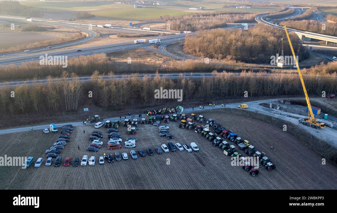 Mainstockheim, Deutschland. Januar 2024. Ein Traktor mit der Aufschrift „Landwirtschaft am seidenen Faden“ wird am Autobahnkreuz Biebelried an der Deponie LZR DK0 in Mainstockheim, wo andere Traktoren abgestellt sind, aus Protest gegen die Sparpläne der Bundesregierung von einem Kran hochgezogen. (Foto mit einer Drohne) Credit: Heiko Becker/dpa/Alamy Live News Stockfoto