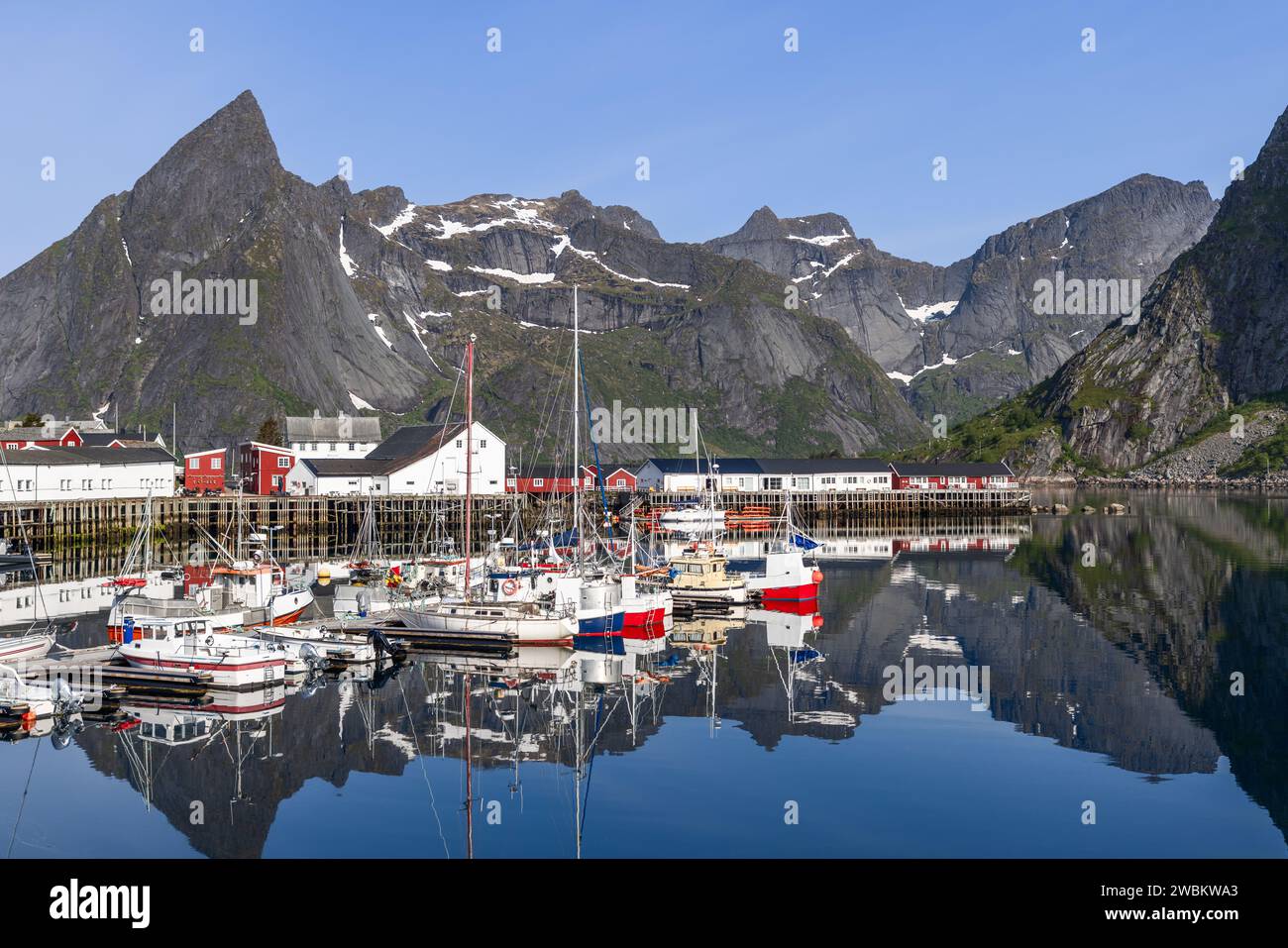 Der beschauliche Hafen von Hamnoy, umgeben von hohen Klippen, zeigt eine unberührte Reflexion von Booten und traditionellen norwegischen Gebäuden. Lofoten Stockfoto