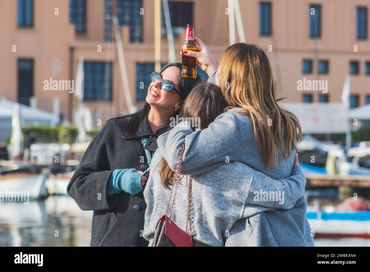 Schöne junge Mädchen trinken Bier und haben Spaß am Pier des kleinen Hafens von Bari, Apulien, Italien mit Booten und Theater im Hintergrund Stockfoto