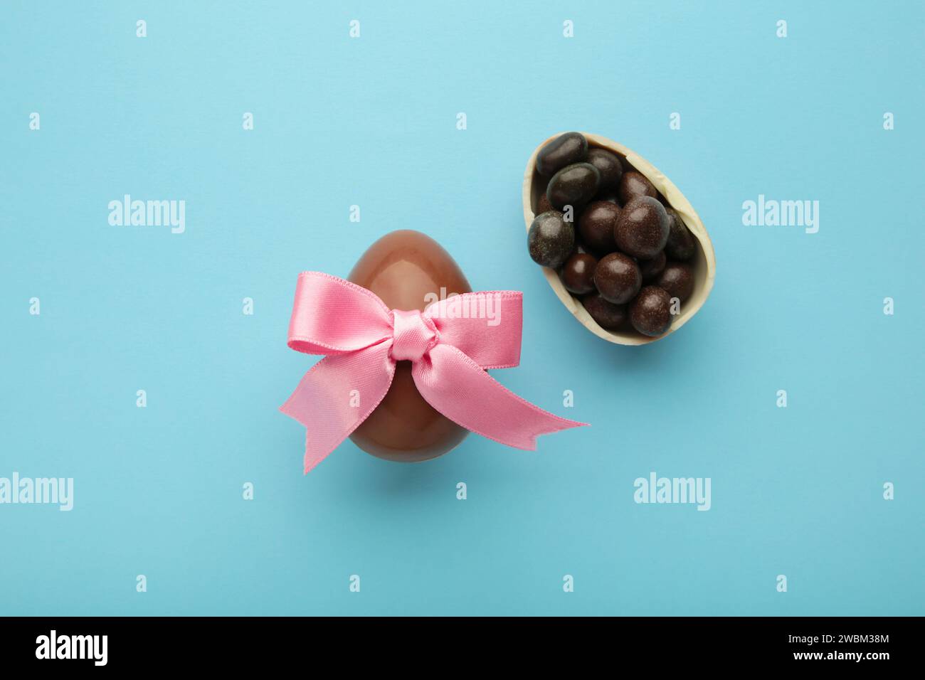 Osterschokolade-Ei mit rosa Schleife auf blauem Hintergrund. Draufsicht Stockfoto