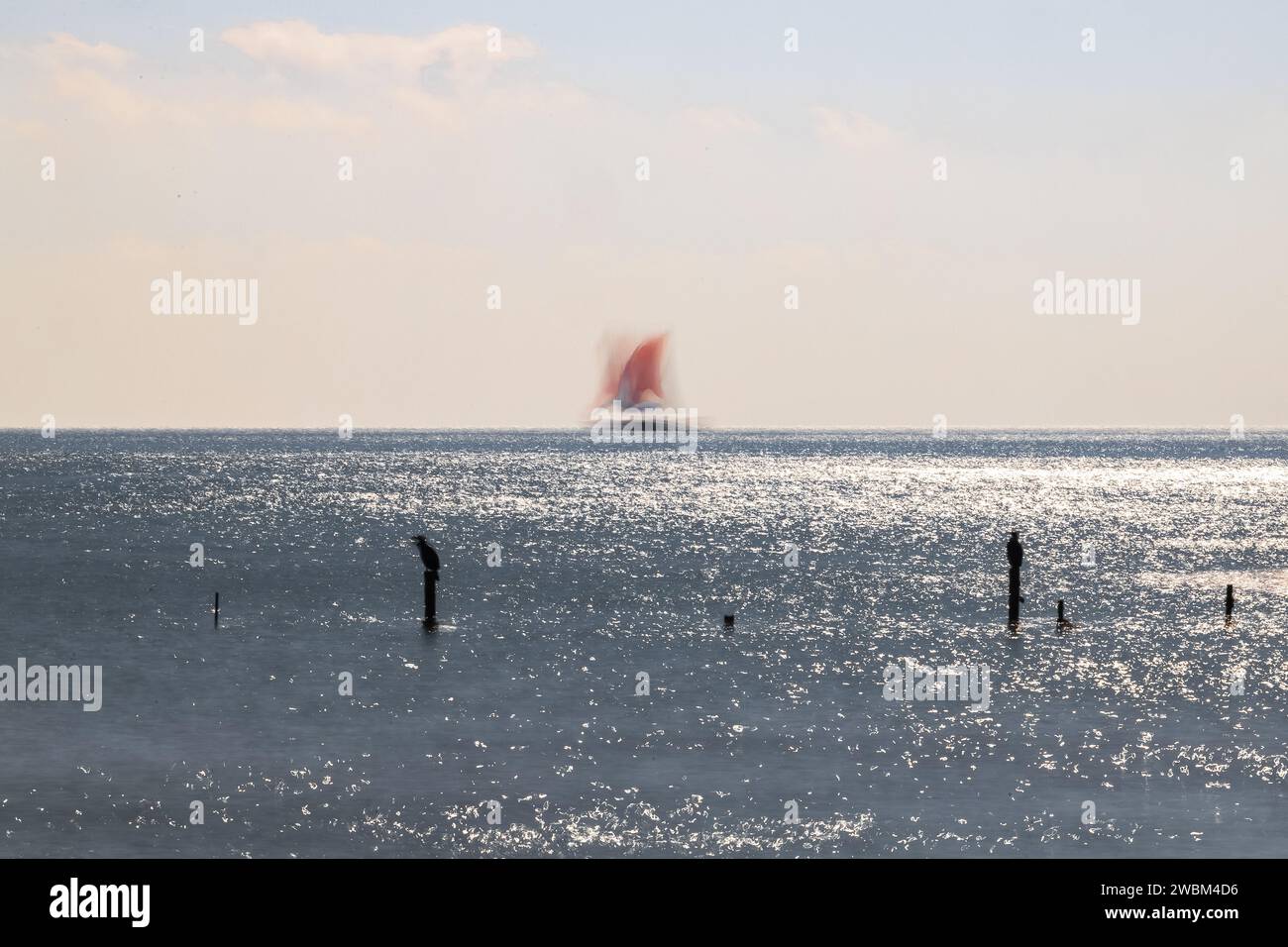 Ein Segelboot, weit weg, frei und glücklich, segelt an einem klaren Wintermorgen über einen hellen Horizont. Stockfoto