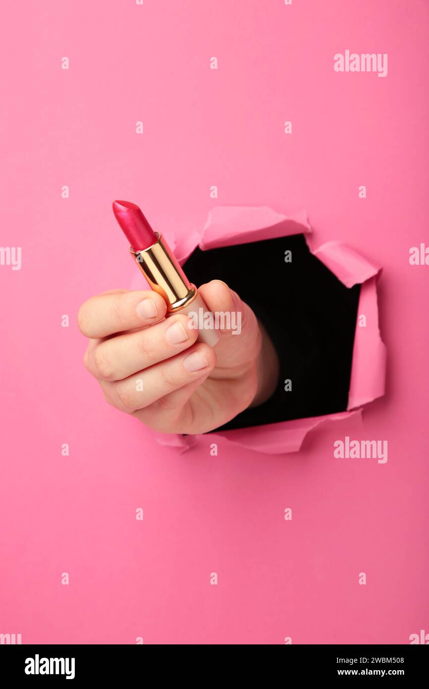Weibliche Hand mit Lippenstift, der durch das rosa Papier schlägt. Draufsicht Stockfoto