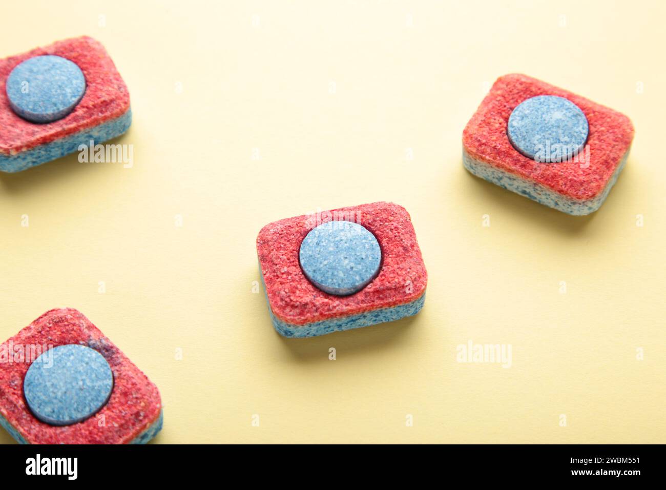 Rote und blaue Tabletten für Geschirrspülmaschinen. Reinigungsmittel für die Haushygiene. Geschirrspülkapseln auf gelbem Hintergrund. Draufsicht Stockfoto