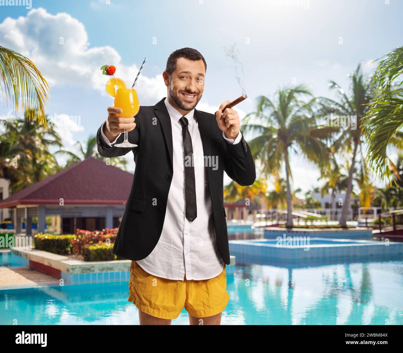 Geschäftsmann in Badeshorts mit Cocktail und Zigarre, die am Pool posiert Stockfoto