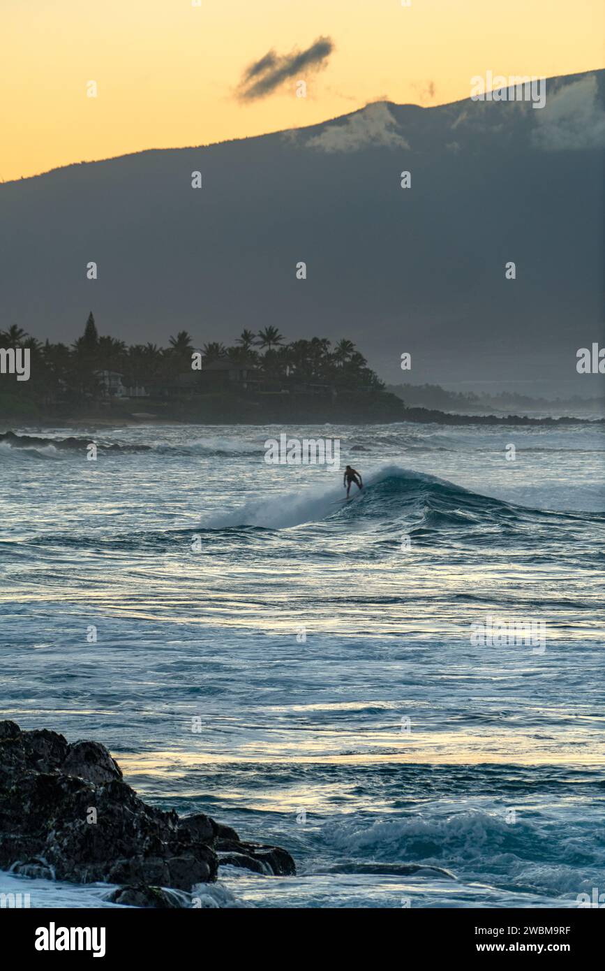 Gegen Mauis verblasstes Licht findet ein Surfer Einsamkeit im Rhythmus der Wellen bei Ho'okipa. Stockfoto