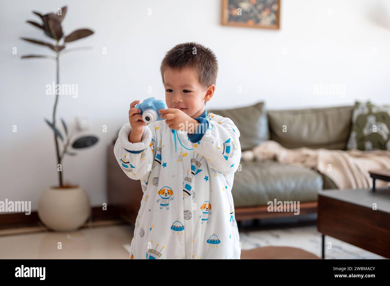 Charmanter zweieinhalb Jahre kleiner Junge, der Spaß beim Spielen und Fotografieren mit einer digitalen Kinderkamera im Wohnzimmer zu Hause hat Stockfoto