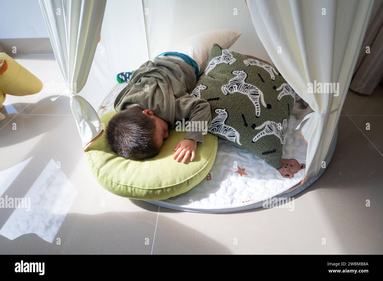 Nach dem Spielen schläft ein süßer zweieinhalb Jahre alter Junge sorglos zwischen weichen Kissen in einem weißen Kinderzelt zu Hause. Gemütliches Nickerchen Stockfoto