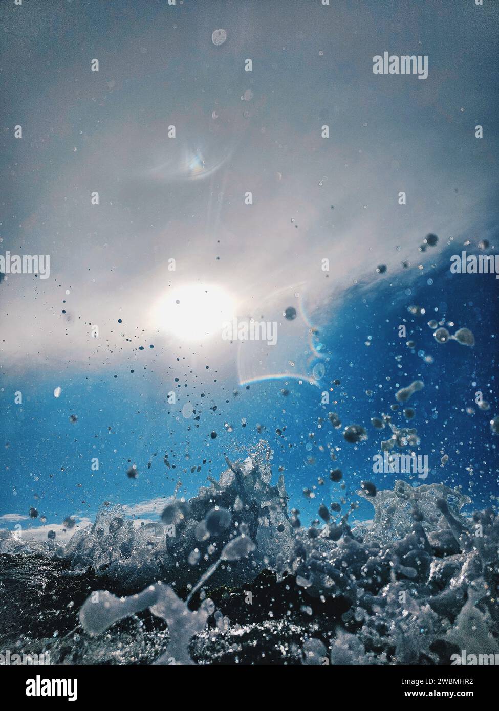 Eine majestätische Welle stürzt vor der atemberaubenden Kulisse eines hellblauen Himmels, der von der Sonne beleuchtet wird Stockfoto