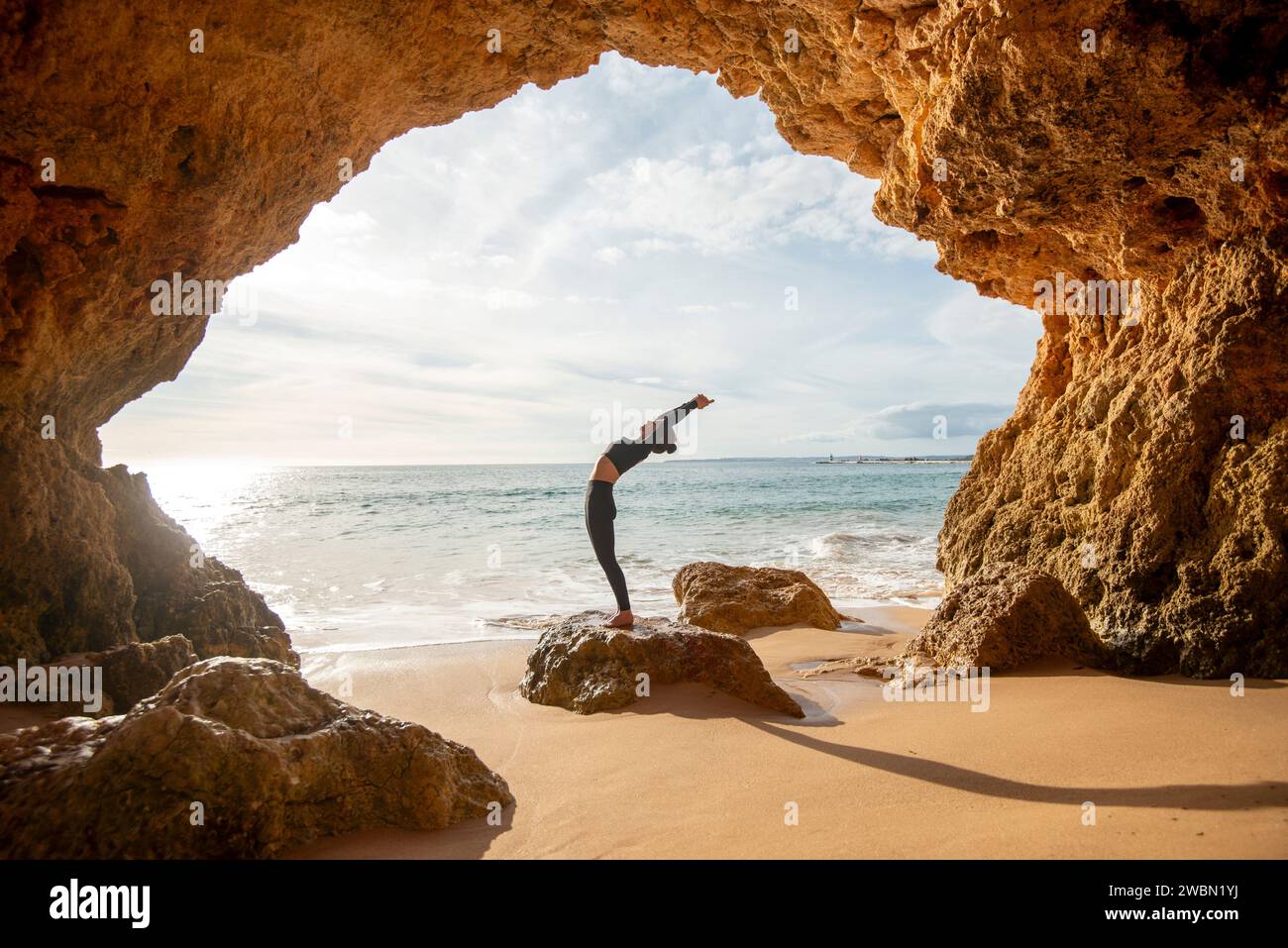 Sportliche Frau, die in einer Höhle am Meer eine Rückenbeugung macht Stockfoto