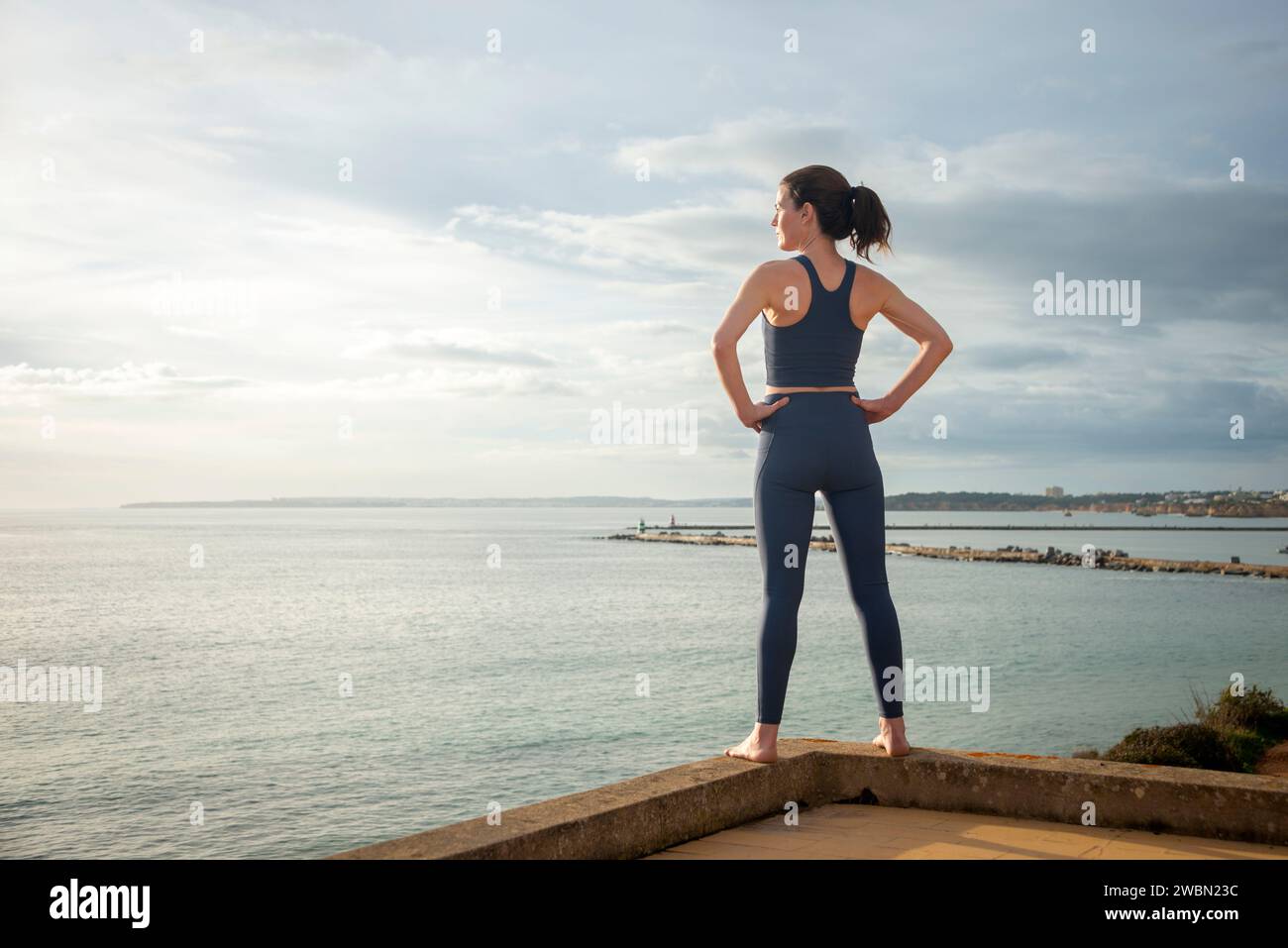 Rückansicht einer sportlichen Frau mit Blick auf das Meer mit Händen auf den Hüften, entspannend nach dem Training. Stockfoto