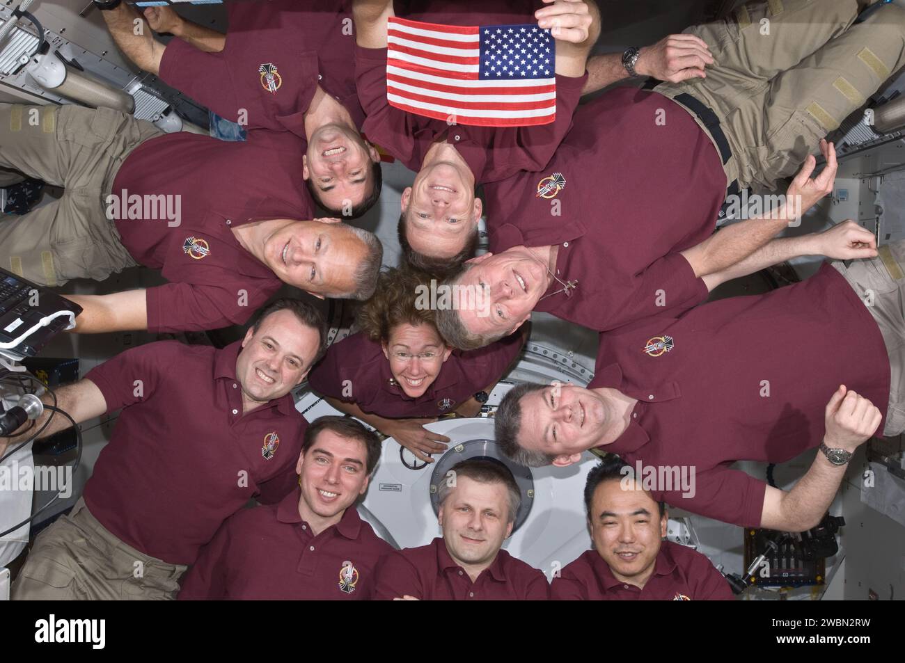 STS-135 Atlantis Crew und Expedition 28 Astronauten an Bord des Kibo-Labors der Internationalen Raumstation bilden einen Schwerelosigkeit-Kreis für ein Porträt. Zu den Crew-Mitgliedern gehören Chris Ferguson, Doug Hurley, Sandy Magnus, Rex Walheim, Satoshi Furukawa, Ron Garan, Mike Fossum, Andrey Borisenko, Alexander Samokutyaev und Sergej Wolkow. Die US-Flagge, die auf STS-1 geflogen ist, wird im Hochformat angezeigt. Stockfoto