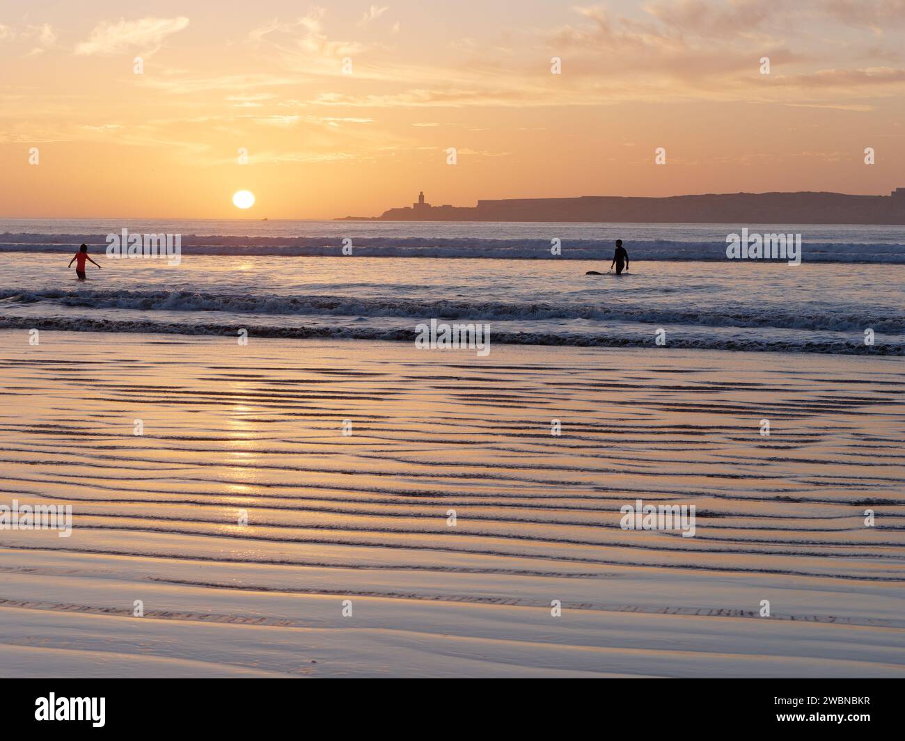 Schwimmen und surfen Sie auf dem Meer, um den Sonnenuntergang am Horizont neben einer Insel in Essaouira, Marokko, am 11. Januar 24 zu genießen Stockfoto