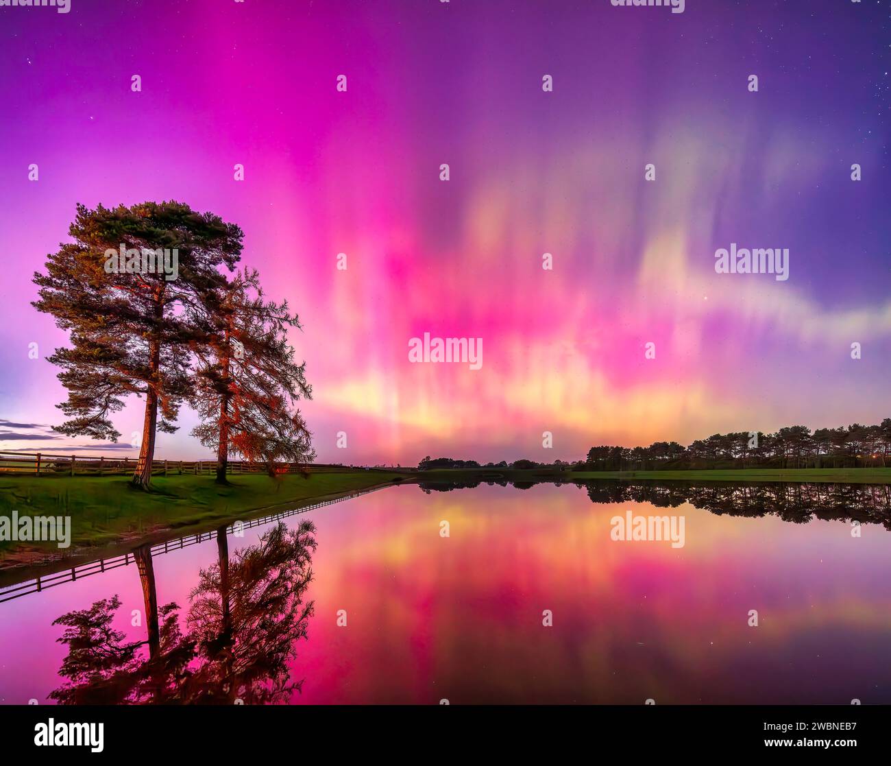 Ein farbenfroher Blick auf die Nordlichter Aurora Borealis spiegelt sich im Whittle Dene Reservoir in Northumberland unter klarem Winterhimmel wider Stockfoto