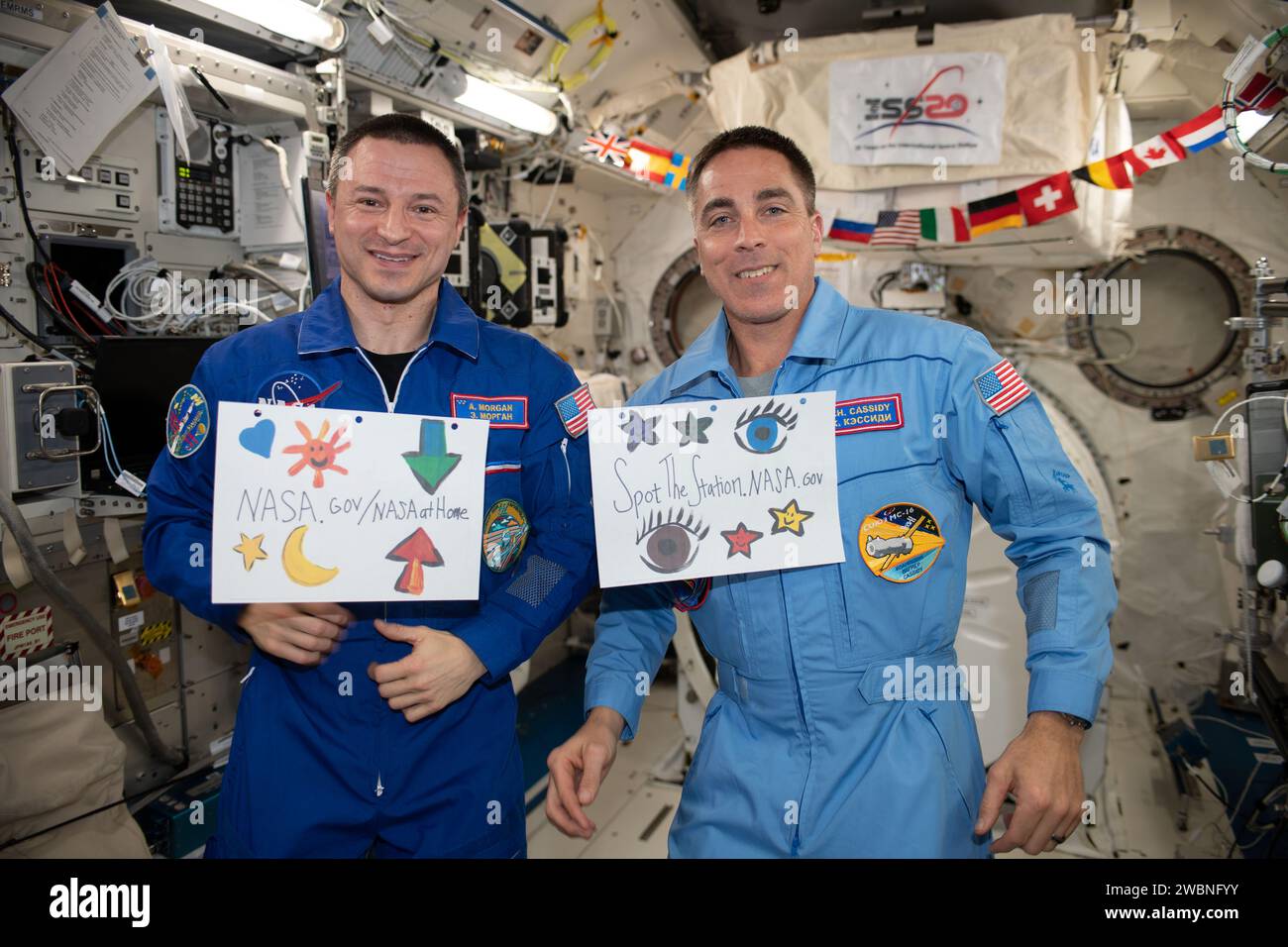 Iss062e147663 (12.04.2020) --- Ein Blick, der während der PAO-Veranstaltung im japanischen Experiment-Modul (JEM) an Bord der Internationalen Raumstation (ISS) aufgenommen wurde. Astronaut Drew Morgan nimmt in seinem blauen Fluganzug an der Veranstaltung Teil. Er hält ein Schild mit der Aufschrift NASA.gov/NASAatHome. Er wird von Astronaut Christopher Cassidy begleitet, der ein Schild mit der Aufschrift Spot the station.NASA.gov hält. Stockfoto