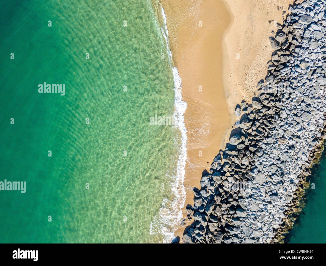 Aus der Vogelperspektive auf den smaragdgrünen Ozean an einem Sandstrand mit einem felsigen Steg Stockfoto