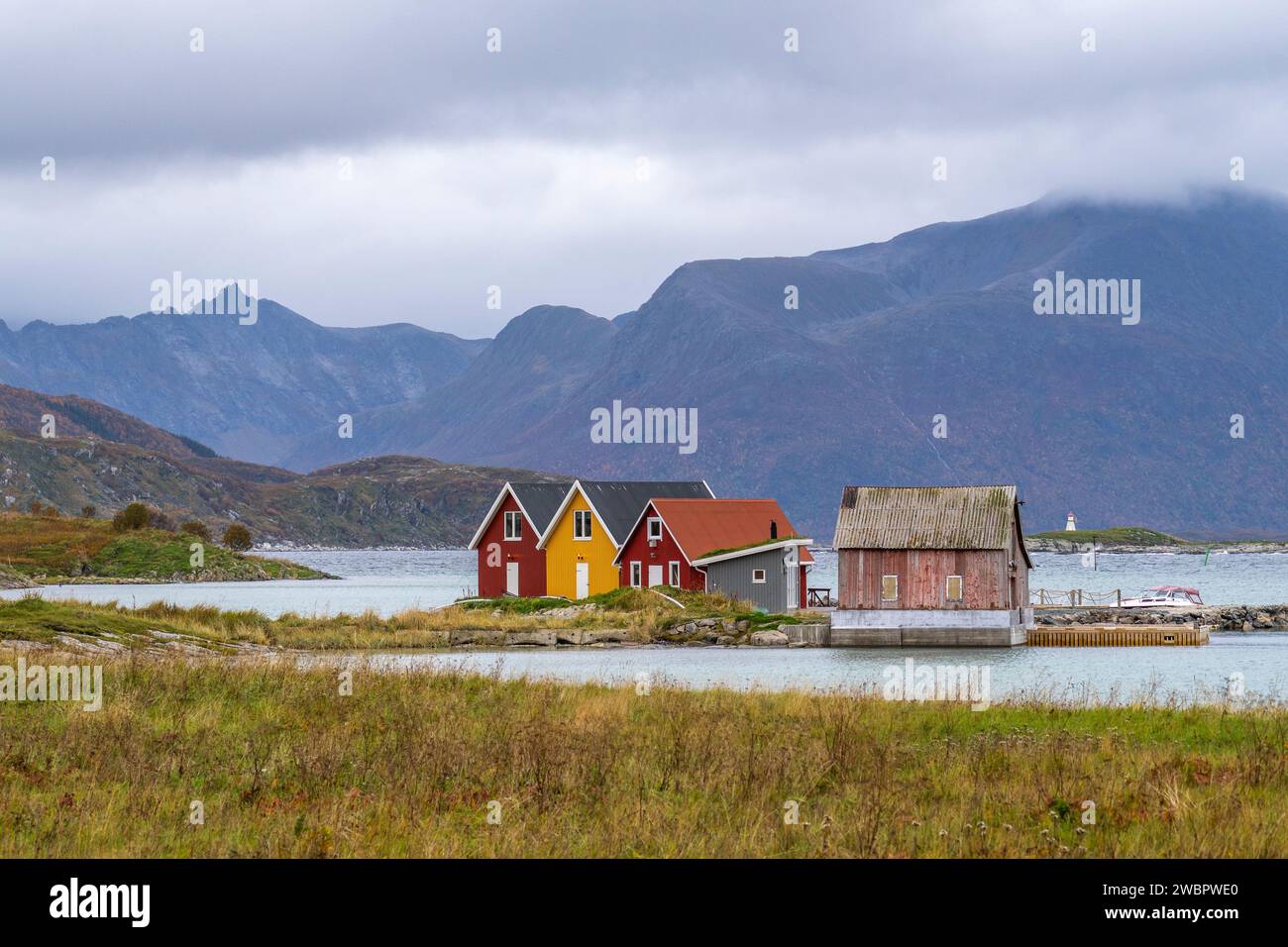 rote und gelbe Häuser am Strand des Atlantik auf der Insel Hillesøya bei Sommarøy, Troms, Norwegen. Landschaft Kalenderfoto mit Bergen im Hintergrund Stockfoto