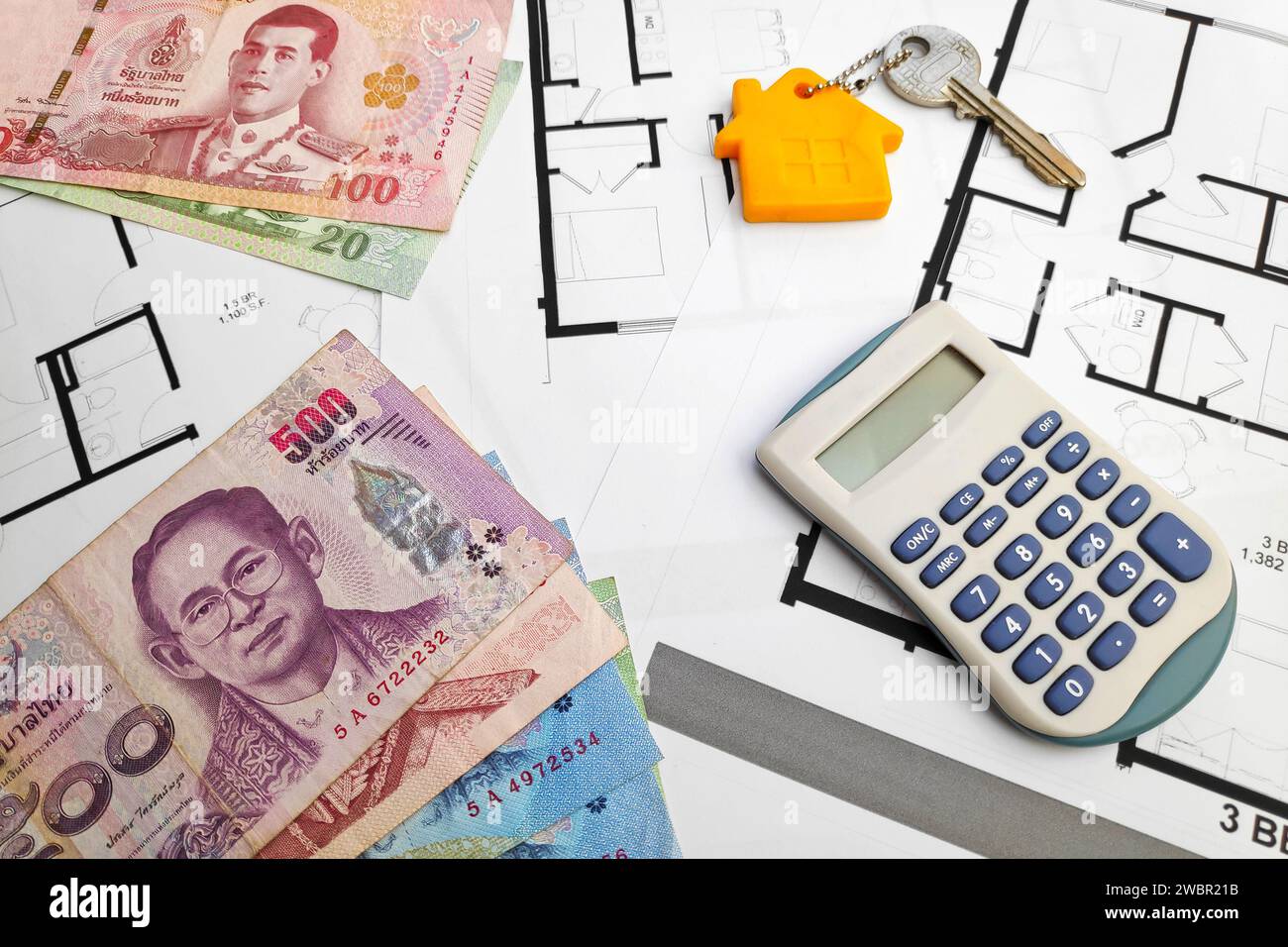 Nahaufnahme einiger thailändischer Baht-Banknoten, eines Hausschlüssels und eines Taschenrechners oben auf den Bauplänen. Stockfoto