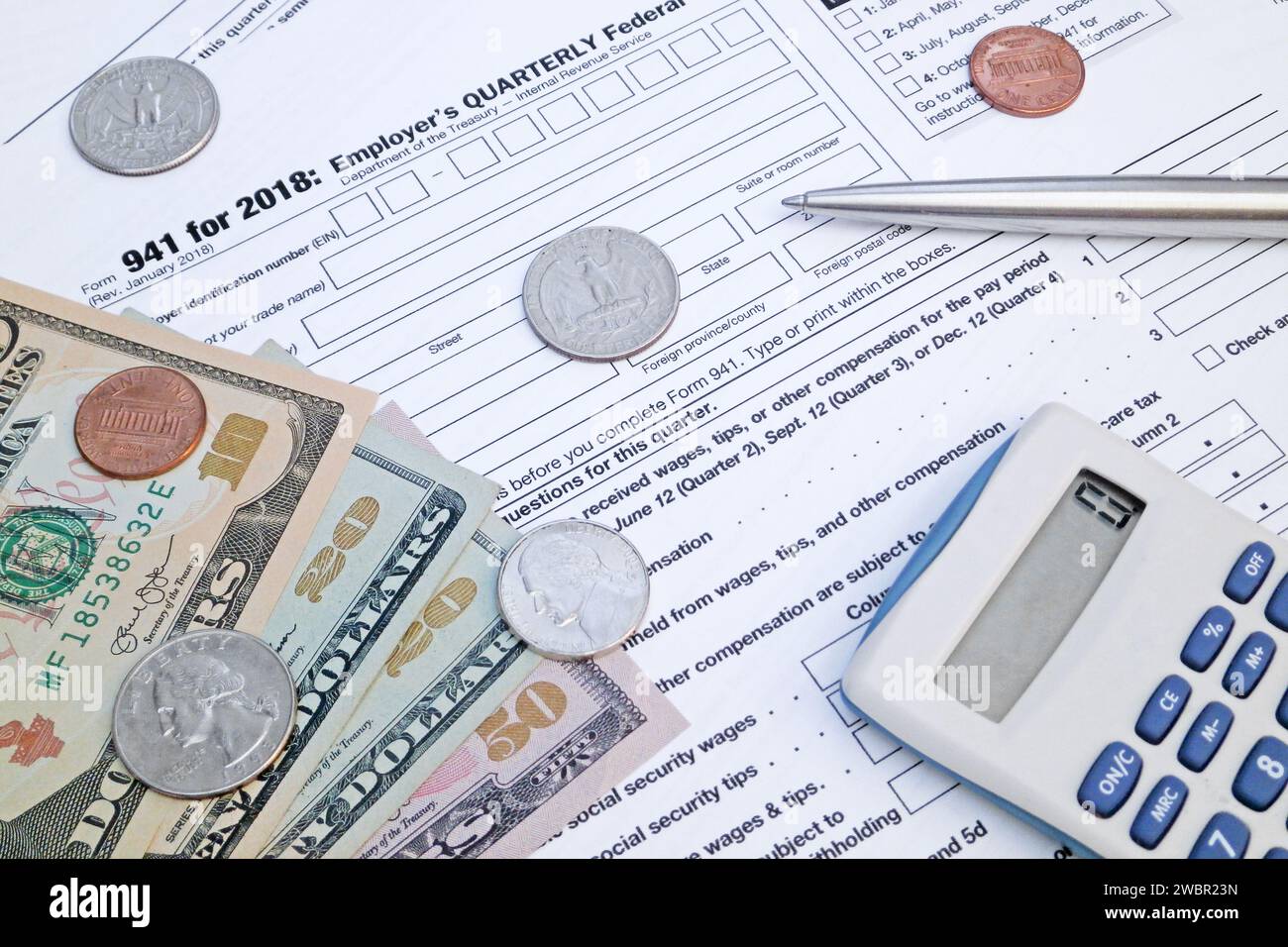 Ein Taschenrechner, ein Stift und einige US-Dollar-Münzen und -Banknoten oben auf dem Formular „vierteljährliche Steuererklärung des Arbeitgebers“. Stockfoto