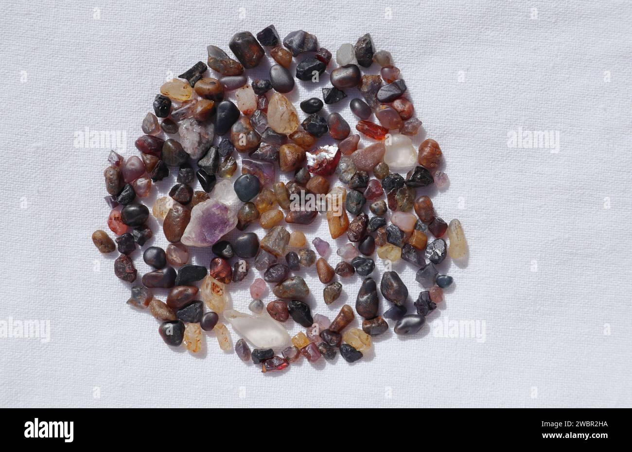 Blick von oben auf eine Vielzahl unbehandelter rauer Edelsteine in verschiedenen Farben und Formen auf weißem Hintergrund Stockfoto