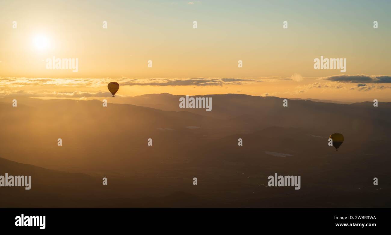 Eine lebendige Szene mit Heißluftballons, die bei Sonnenaufgang über majestätische Berggipfel gleiten Stockfoto