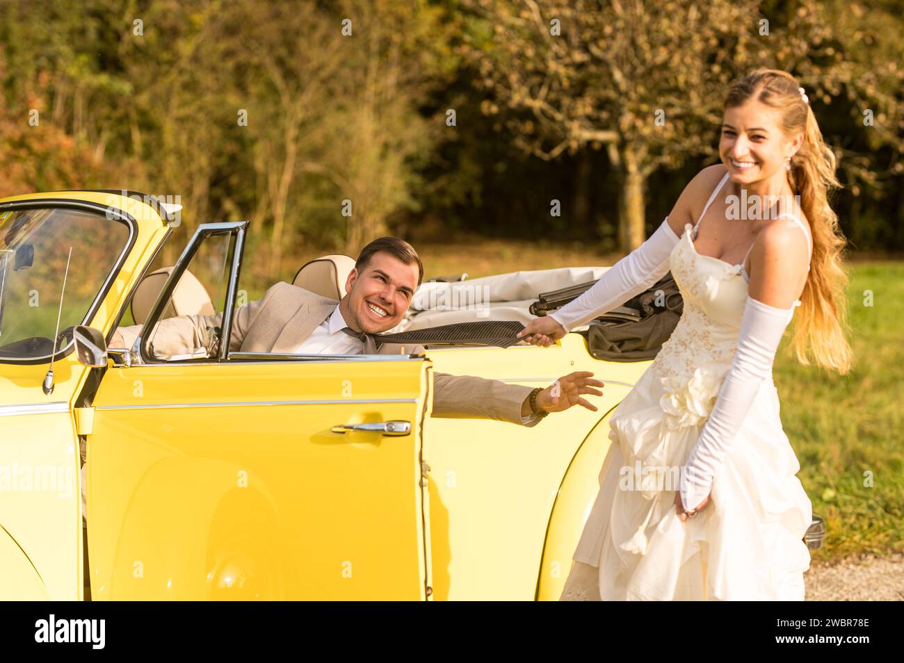 Lustige, ungewöhnliche, stilvolle, originelle Fotos mit Rollenumkehr eines jungen, attraktiven Brautpaares mit wunderschönen Veteranenautos in der Natur. Stockfoto