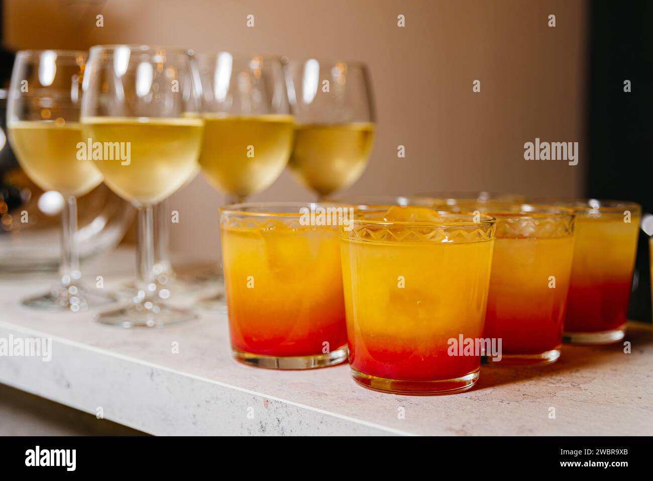 Eine Auswahl an Tequila Sunrise Cocktails mit Orangenverläufen und Weißwein in Stielgläsern, bereit für eine Party. Stockfoto