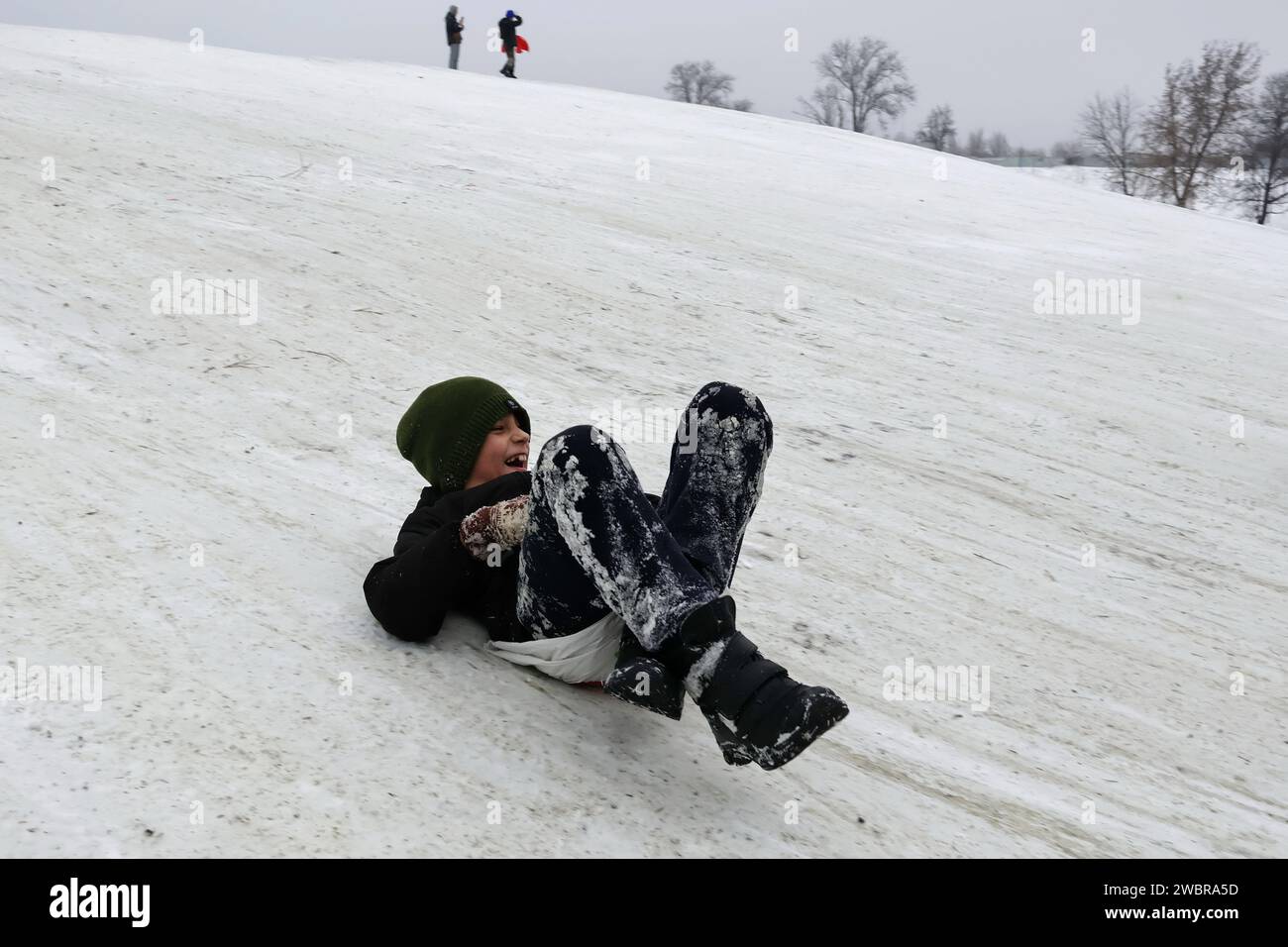 Ein Kind, das von einem Schneehügel in einem Stadtpark in Zaporischzhia aus Schlittenfahren gesehen wurde. Seit der Eskalation des Krieges im Februar 2022 haben die Kinder und ihre Familien der Ukraine 23 Monate Zwangsvertreibung, undenkbaren Verlusten und unerbittlicher Gewalt ertragen müssen. Seit Beginn des Krieges in der Ukraine sind Kinder zu einer der gefährdetsten Bevölkerungsgruppen geworden. Eine der spürbarsten Auswirkungen des Krieges auf Kinder ist der Verlust von Eltern und Freunden. Viele Kinder werden verwaist oder gezwungen, unter zerstörten Bedingungen zu leben. Stockfoto