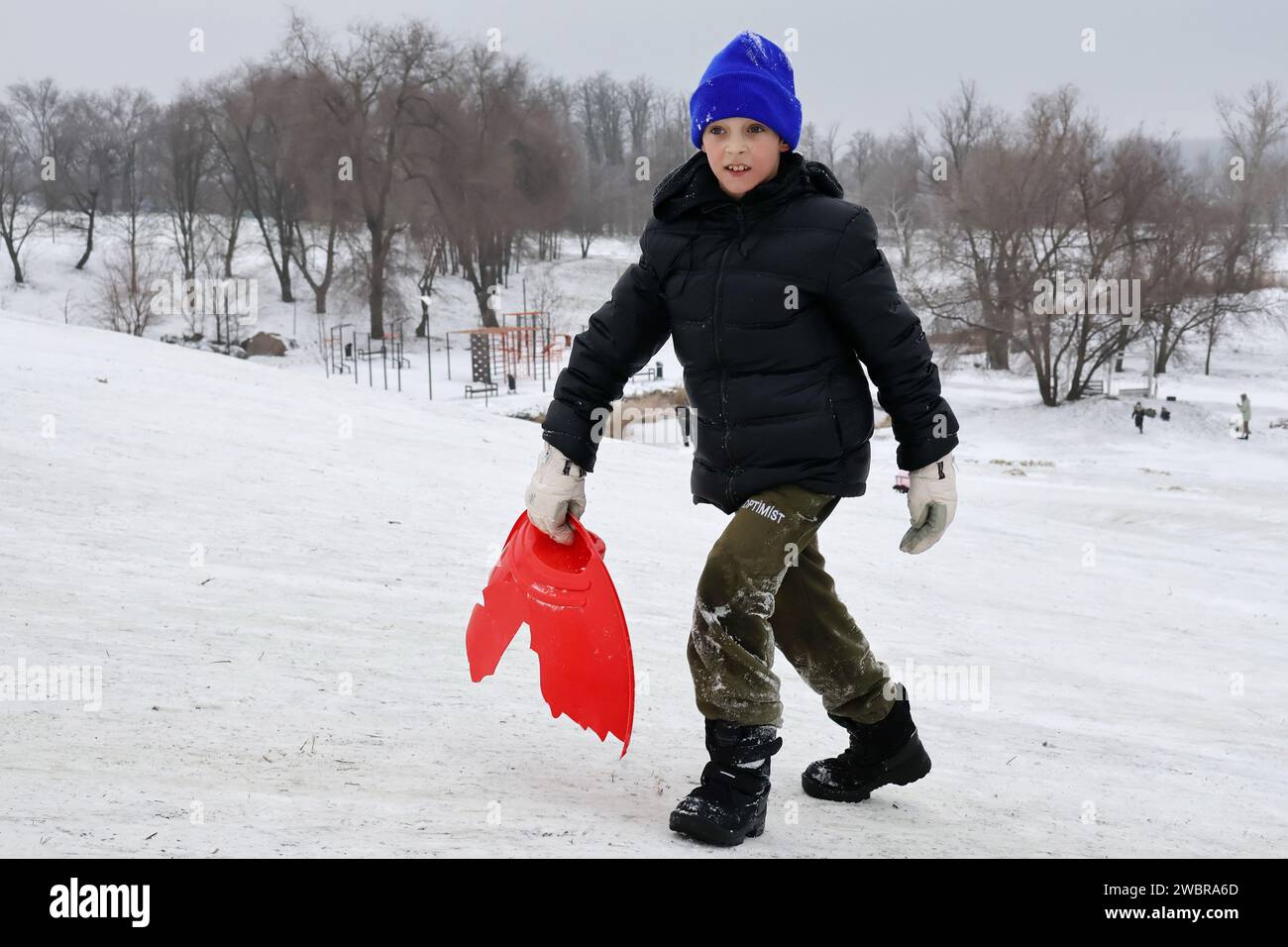 Ein Kind klettert auf den Schneehügel, um in einem Stadtpark in Zaporischzhia Schlitten zu fahren. Seit der Eskalation des Krieges im Februar 2022 haben die Kinder und ihre Familien der Ukraine 23 Monate Zwangsvertreibung, undenkbaren Verlusten und unerbittlicher Gewalt ertragen müssen. Seit Beginn des Krieges in der Ukraine sind Kinder zu einer der gefährdetsten Bevölkerungsgruppen geworden. Eine der spürbarsten Auswirkungen des Krieges auf Kinder ist der Verlust von Eltern und Freunden. Viele Kinder werden verwaist oder gezwungen, unter zerstörten Bedingungen zu leben. Stockfoto