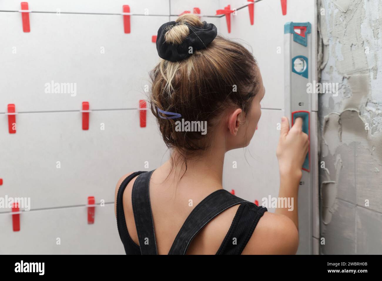 Frau, die die Wände des Badezimmers mit einer Wasserwaage fliesst, um eine Wand auf der Baustelle zu messen. Der Prozess der Installation von Fliesen im Badezimmer Schritt für Schritt Stockfoto